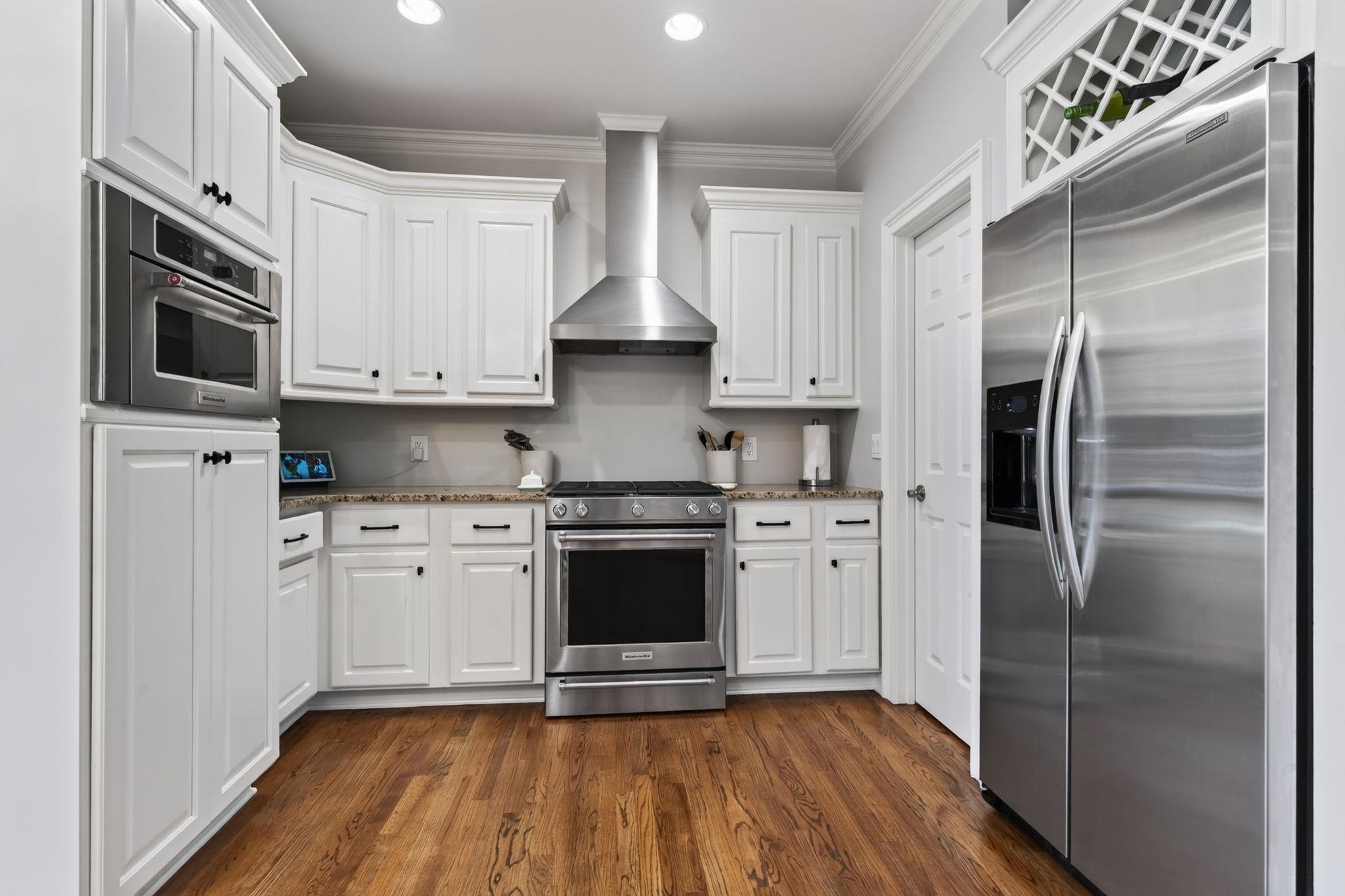Kitchen with white cabinets, stainless steel appliances, granite counters, and warm wood floors.