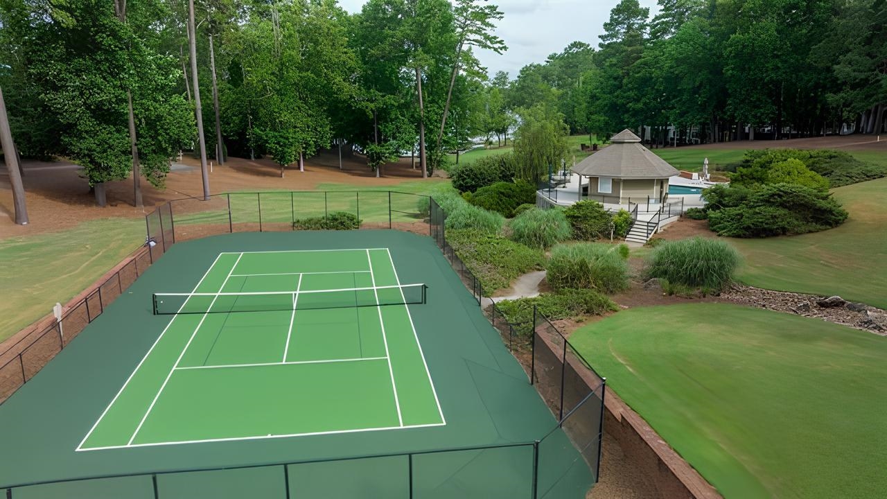 Outdoor tennis court beside a swimming pool and pavilion, surrounded by lawns and mature trees.
