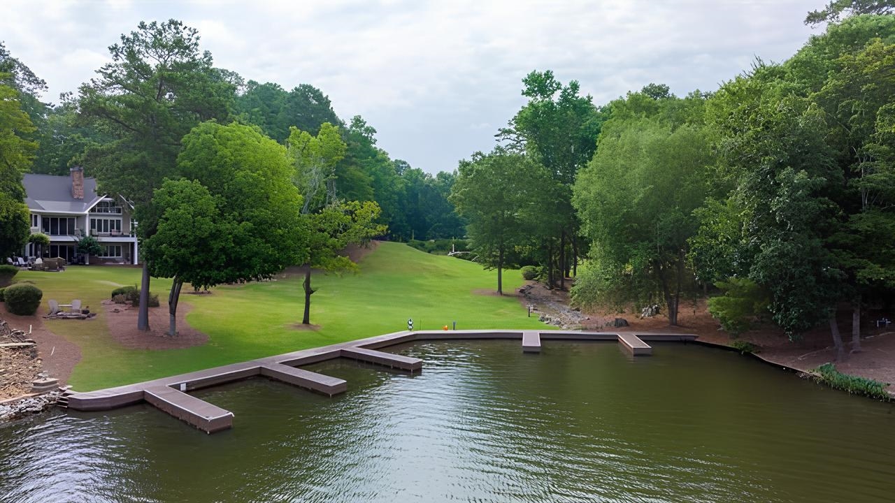 Lakefront property with a long dock, landscaped lawn, mature trees, and a home along the shore.