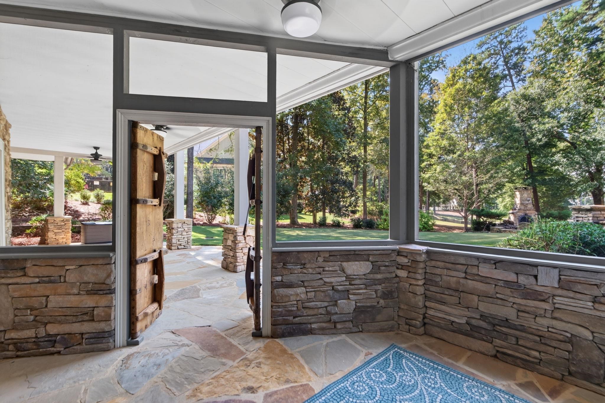 Enclosed porch with stone walls, flagstone flooring, and an open wooden door to a leafy yard.