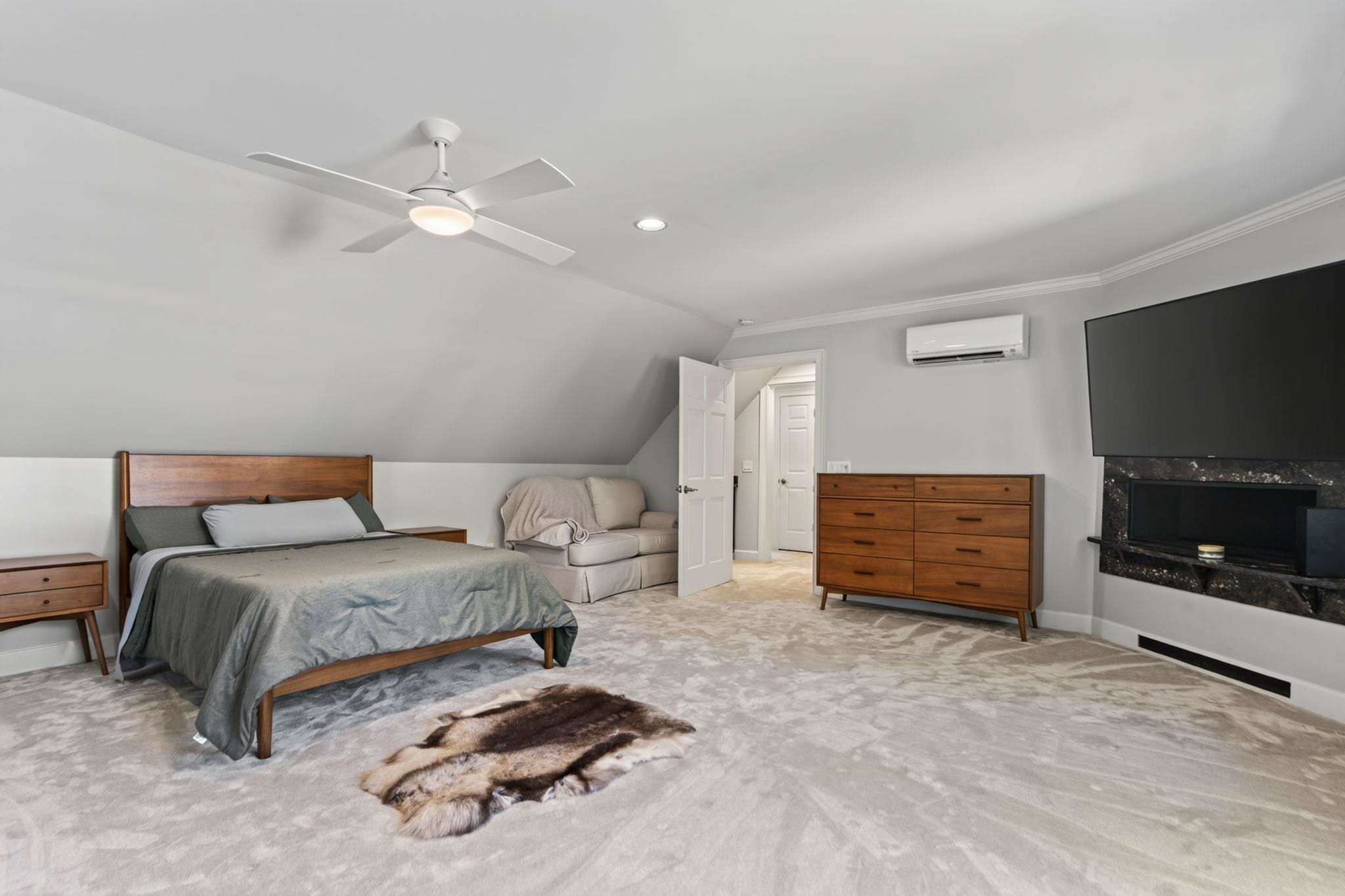 Bedroom with a sloped ceiling, wooden bed, sofa, and fireplace beneath a large television.
