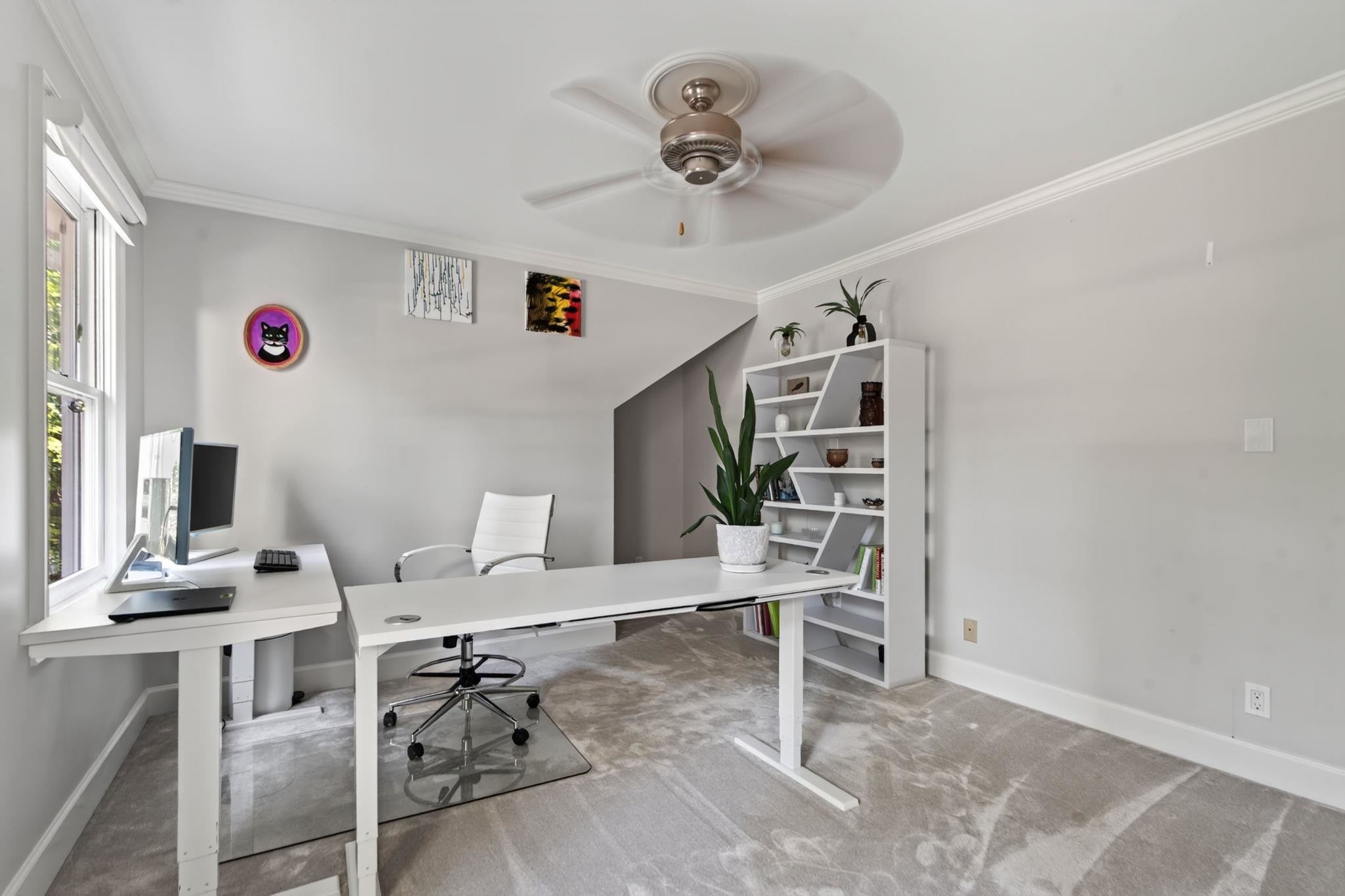 Home office with white desks, a computer, angled shelving, and large windows.