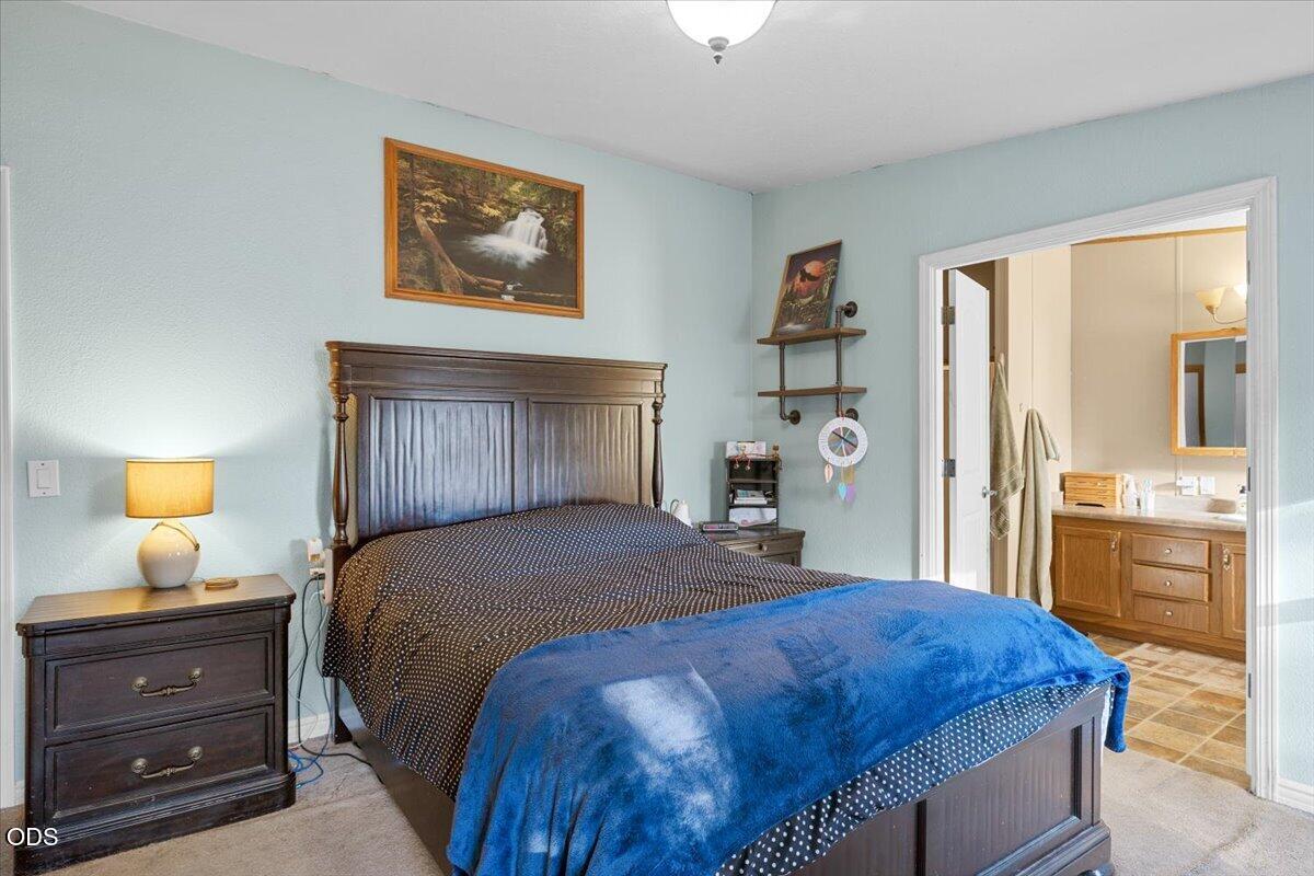 Furnished bedroom with a dark wood bed and blue blanket beside an adjoining bathroom.