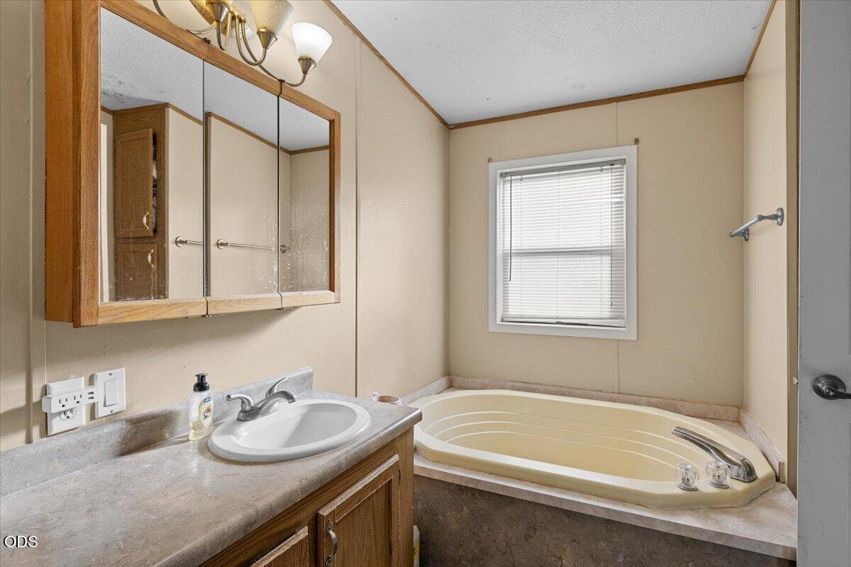 Bathroom with a large jetted tub beside a wood vanity and mirrored medicine cabinet.