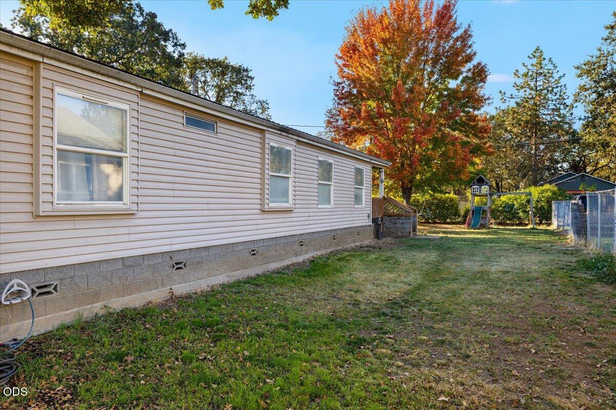 Beige manufactured home beside a grassy backyard with a fenced play area and autumn tree.
