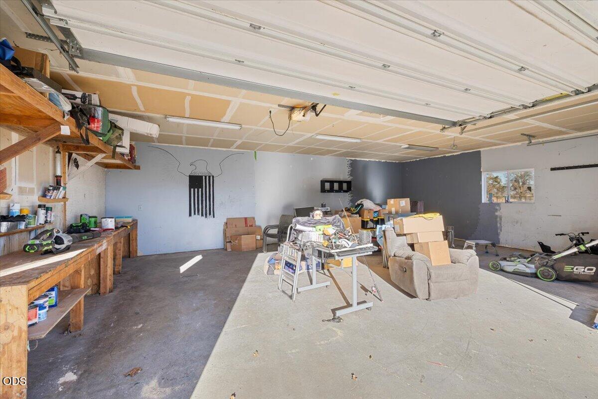 Spacious garage with an open overhead door, wooden workbench, shelves, and stored items.