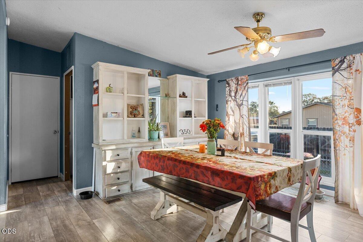 Dining room with a white built-in hutch, patterned tablecloth, and bright windows.