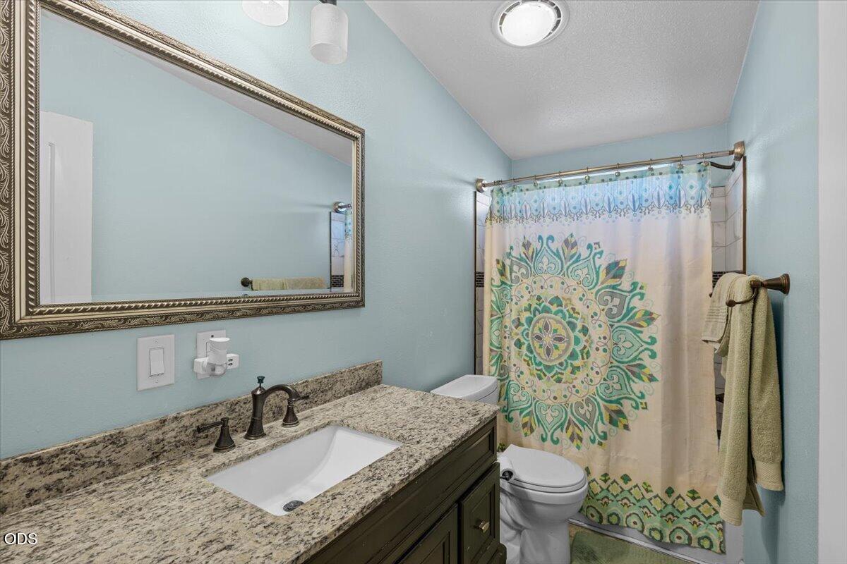 Bathroom with granite vanity, framed mirror, and colorful patterned shower curtain.