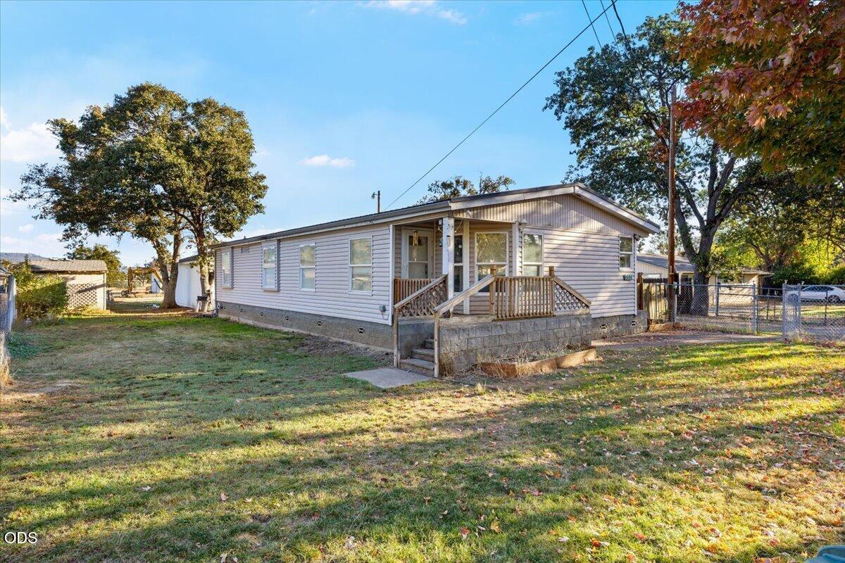 Single-story manufactured home with a raised wooden porch in a grassy, tree-lined yard.