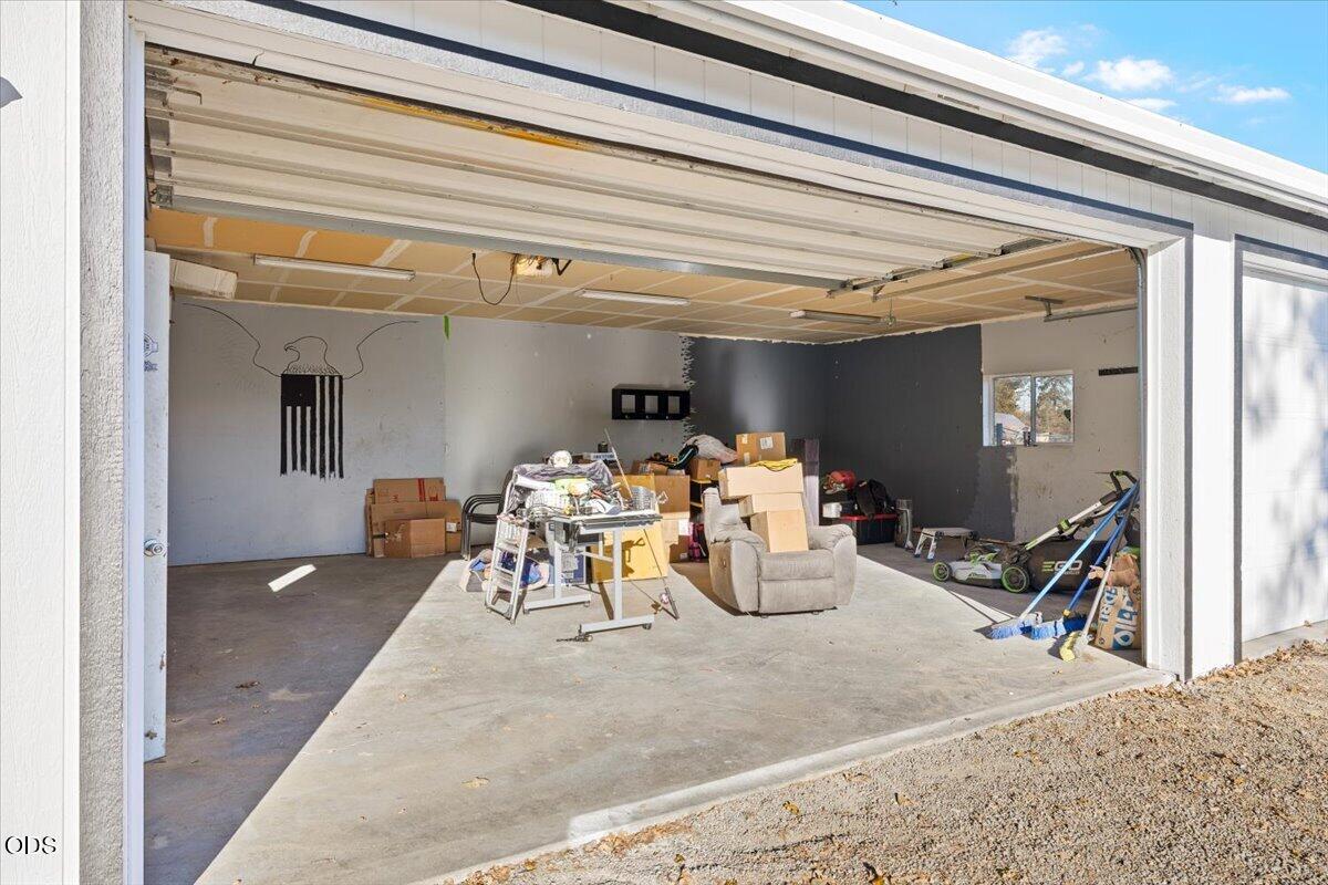Open garage with unfinished ceiling panels, concrete floor, and stored boxes and equipment.