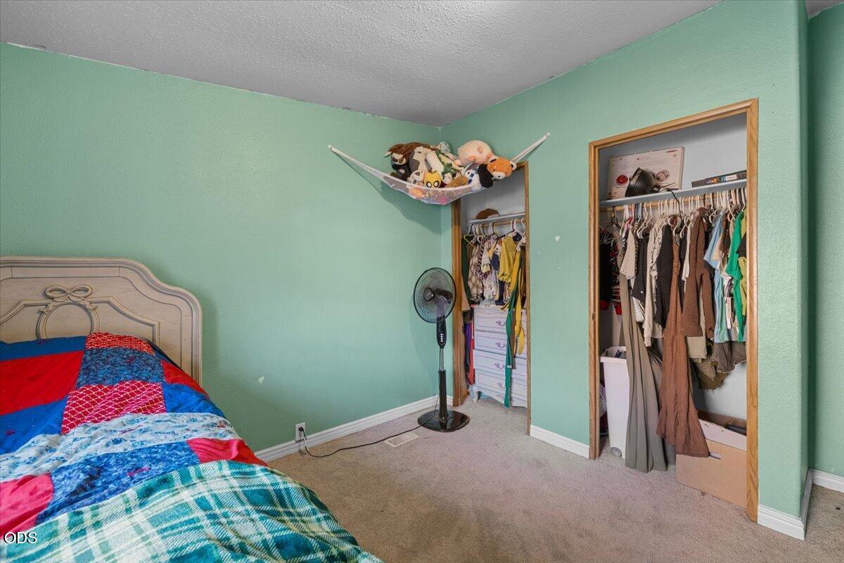 Bedroom with mint-green walls, a colorful bed, and two open clothing-filled closets.