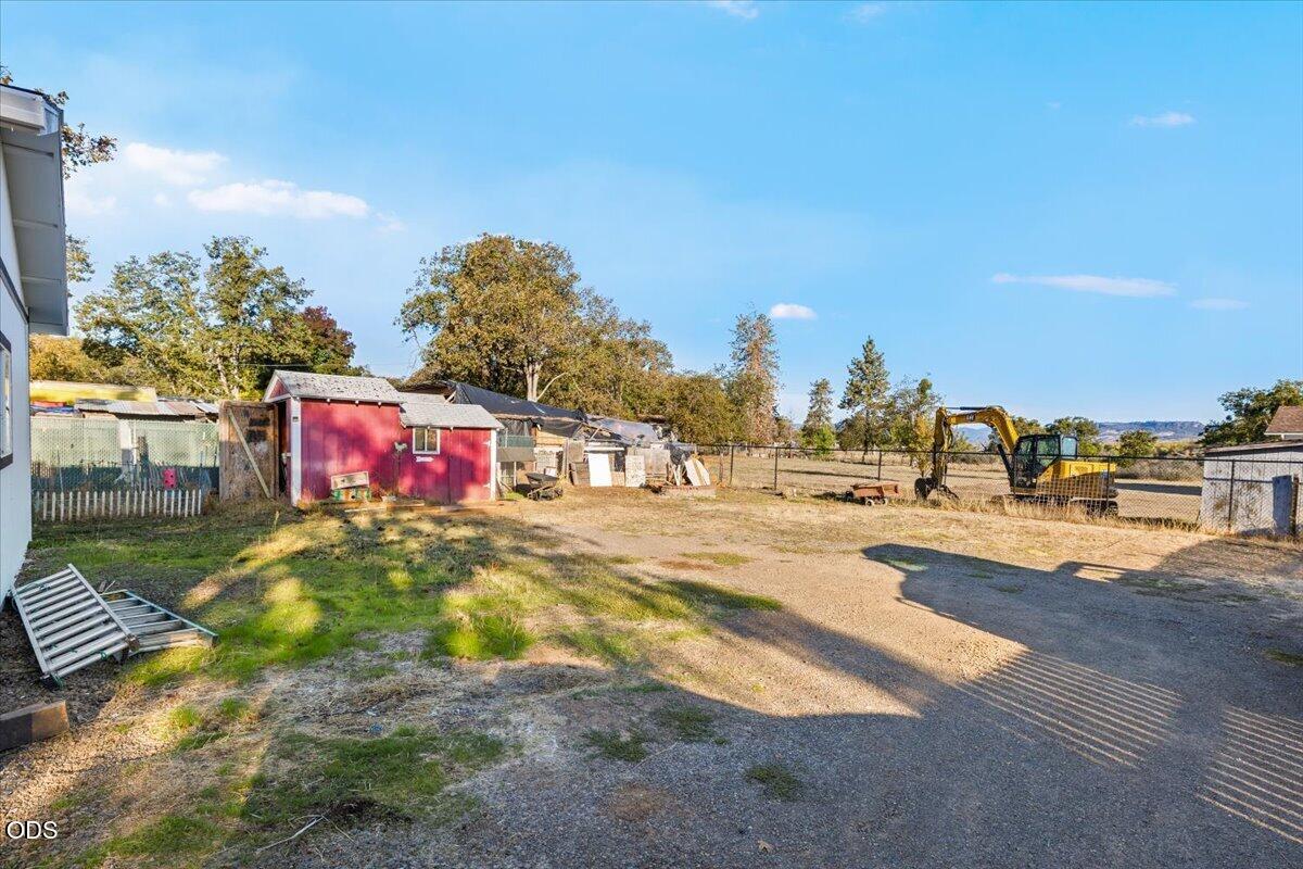 Gravel yard with a red shed, fenced enclosures, and a yellow excavator.