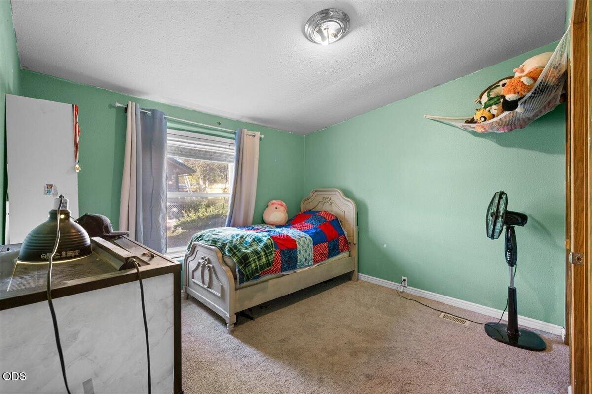 Bedroom with mint-green walls, a single bed with a colorful patchwork quilt, and a curtained window.