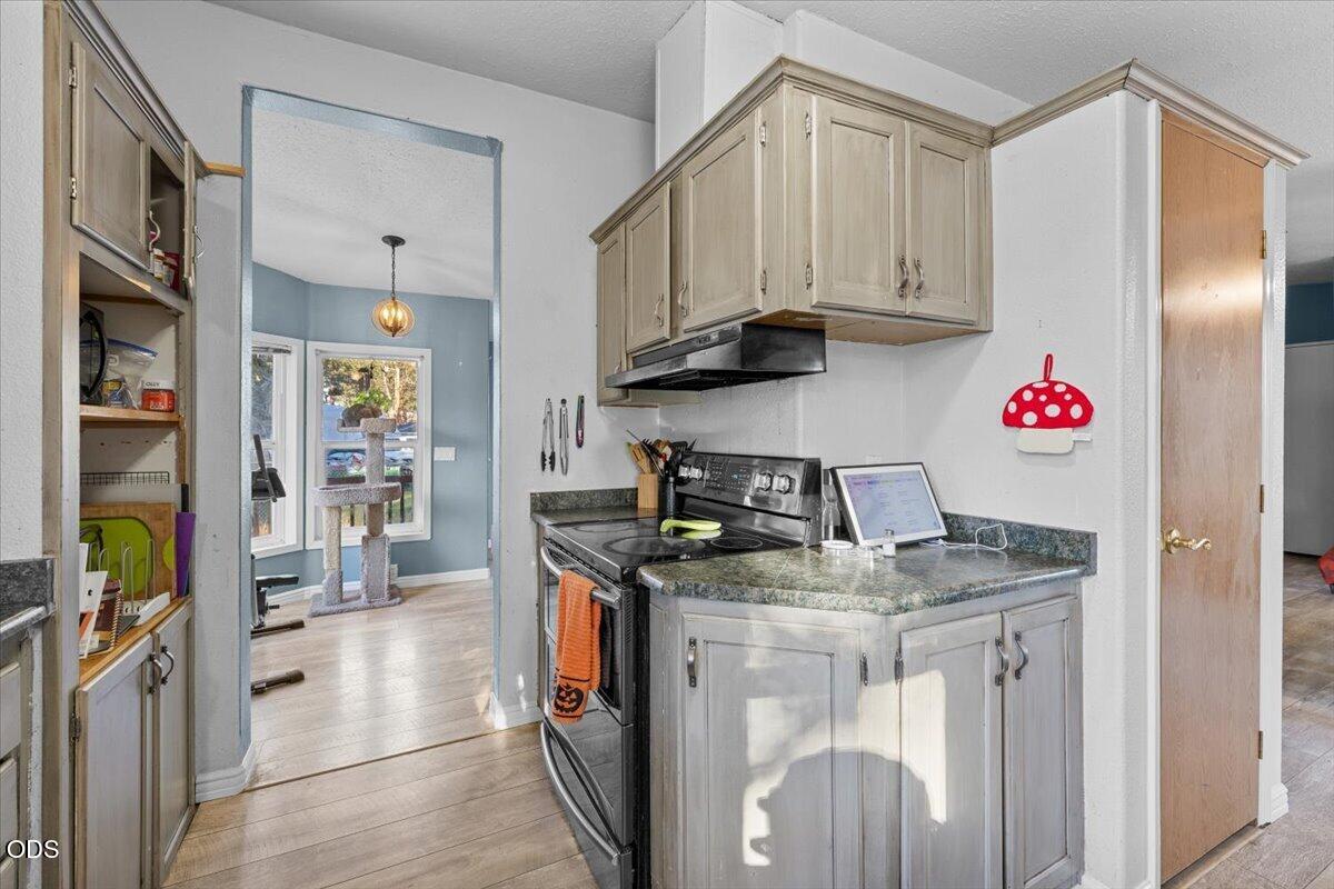 Kitchen with gray cabinetry, granite counters, and a black range beside open pantry shelving.