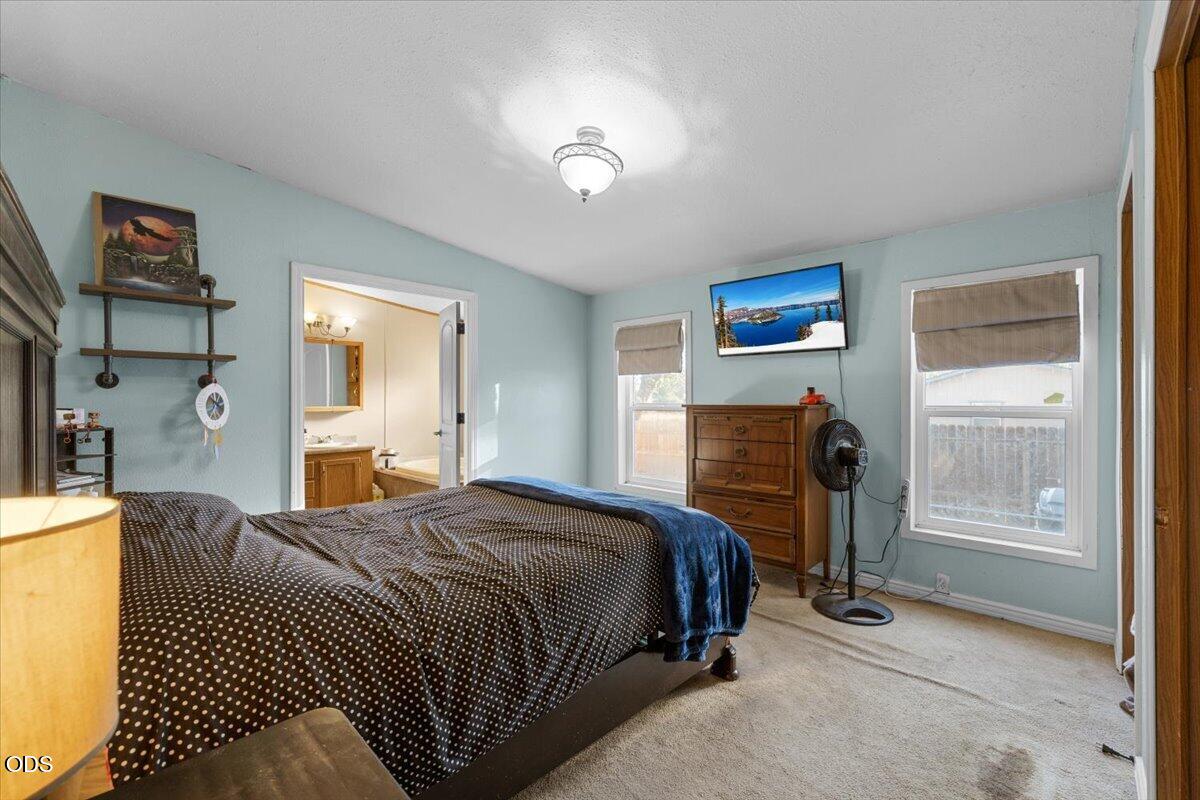 Bedroom with pale blue walls, a patterned bedspread, and an open doorway to the bathroom.