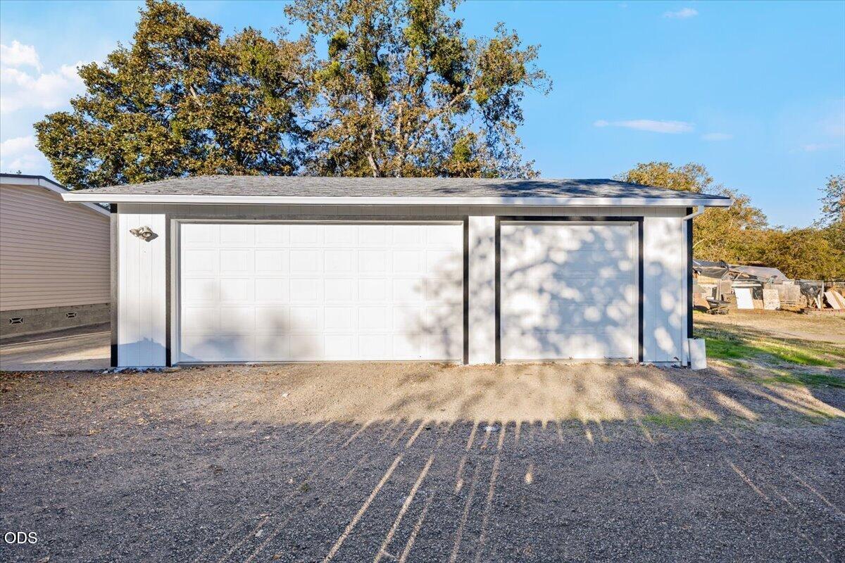 Detached light-colored garage with two large doors and a gravel driveway.