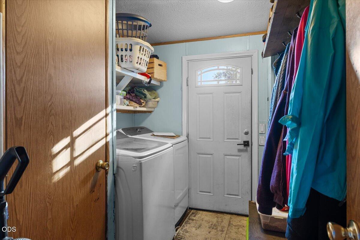 Laundry area with washer and dryer, storage shelves, hanging coats, and a white door.