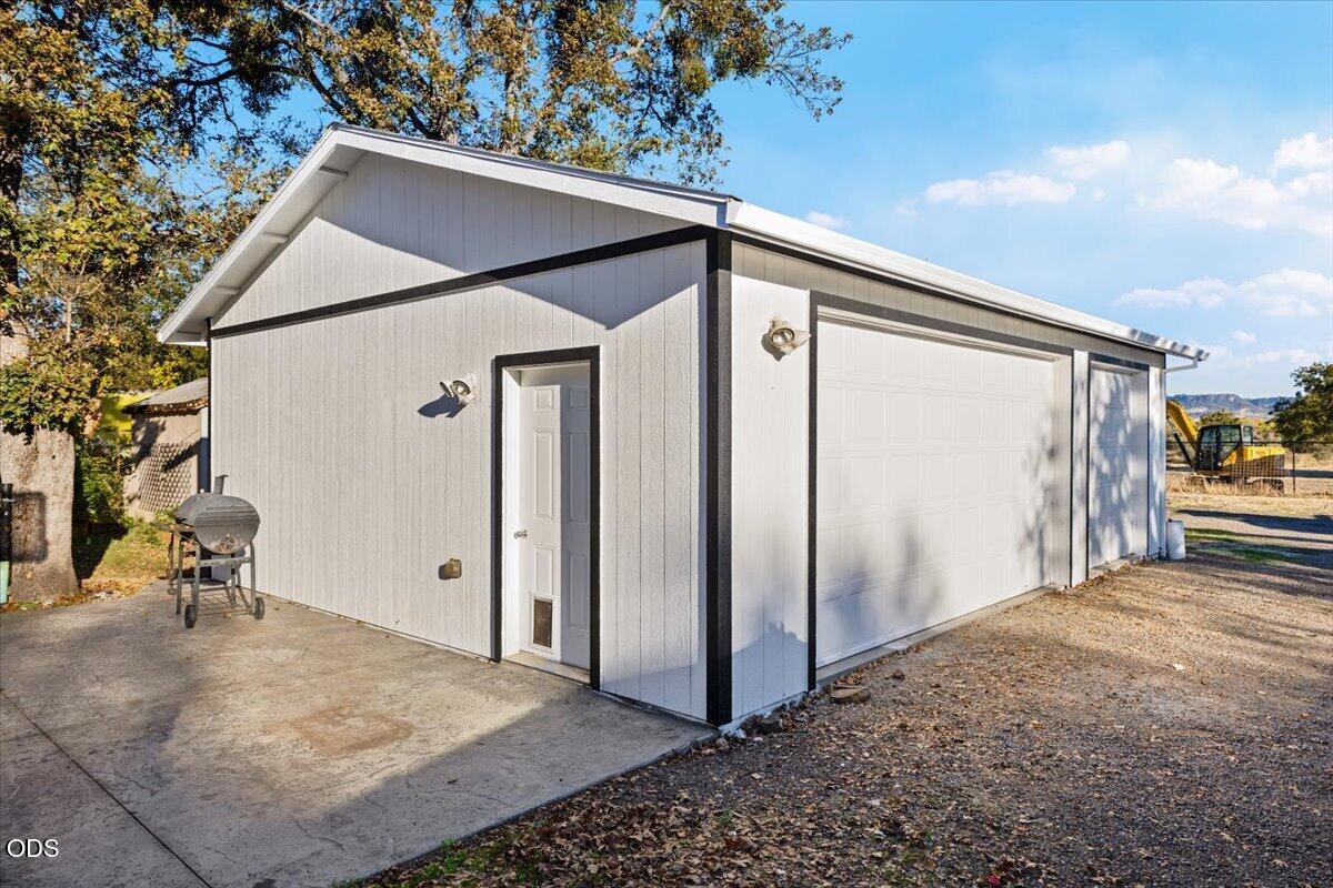 Detached gray garage with black trim, a white side door, and a wide double garage door.