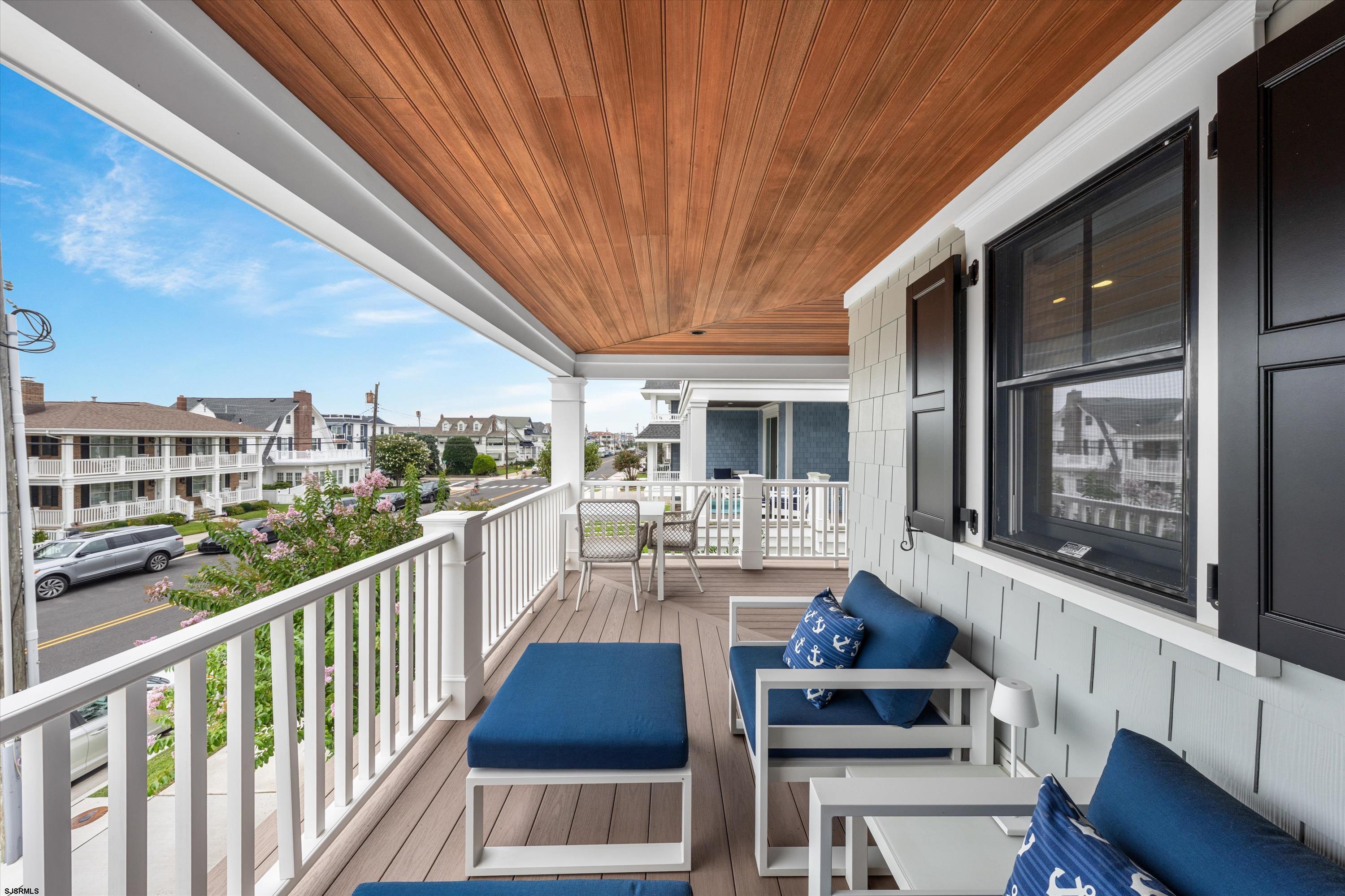 Covered porch with a wood ceiling and blue seating overlooking a residential street.