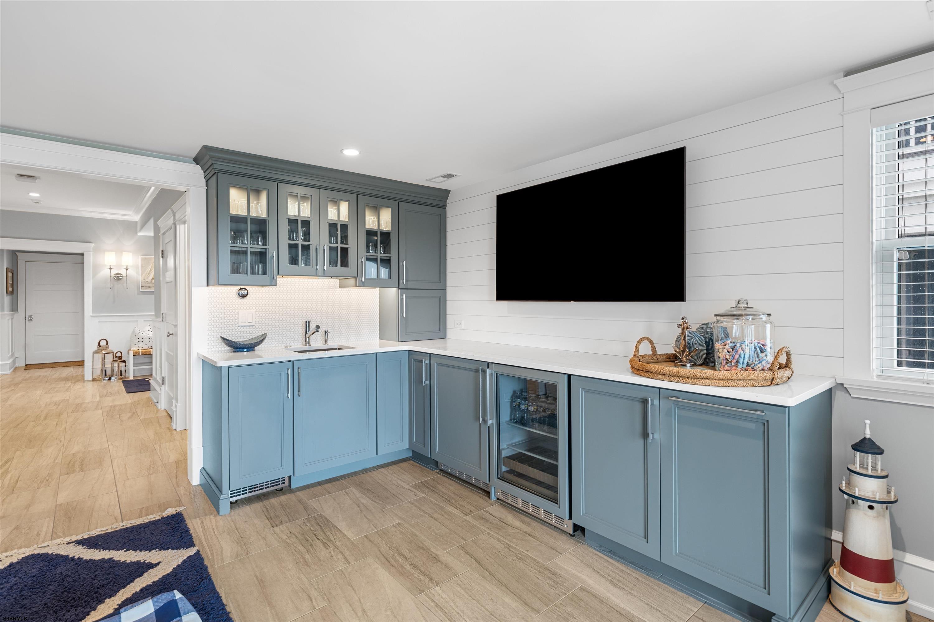 Built-in wet bar with blue-gray cabinets, a glass-front beverage refrigerator, and a large wall-mounted TV.