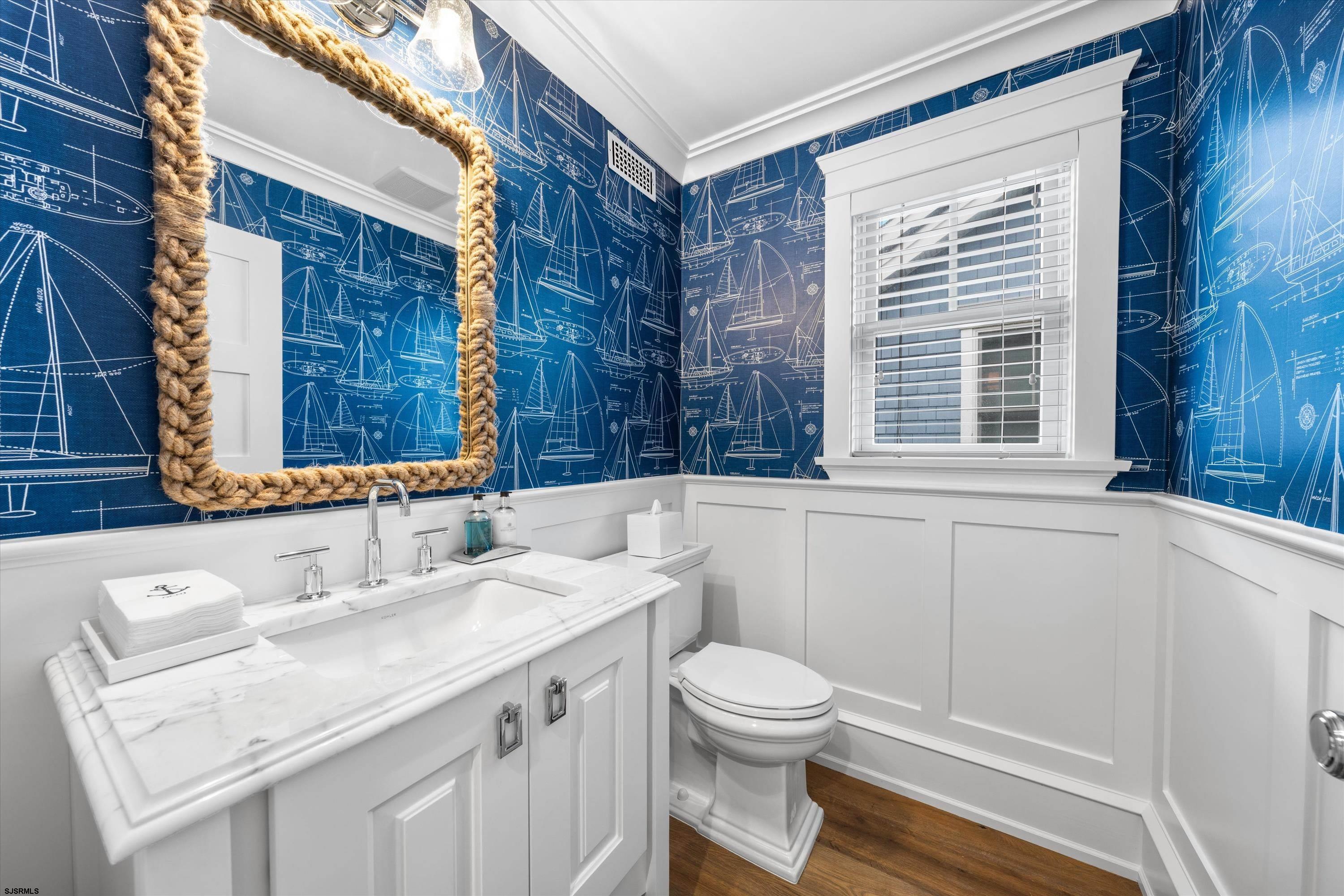 Bathroom with sailboat-patterned navy wallpaper, a rope-framed mirror, and a white marble vanity.