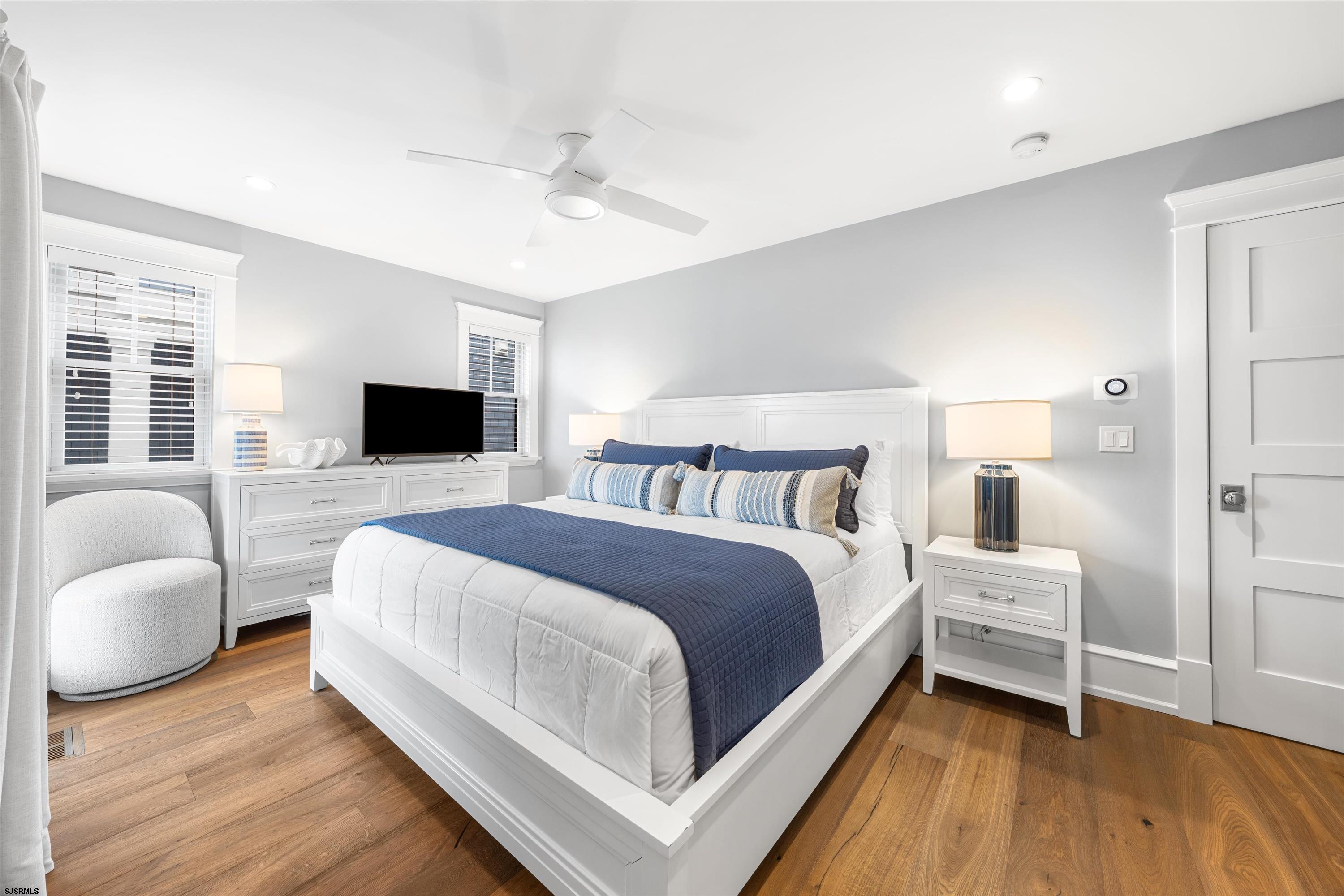 Furnished bedroom with a white bed, navy bedding, matching lamps, and warm wood floors.