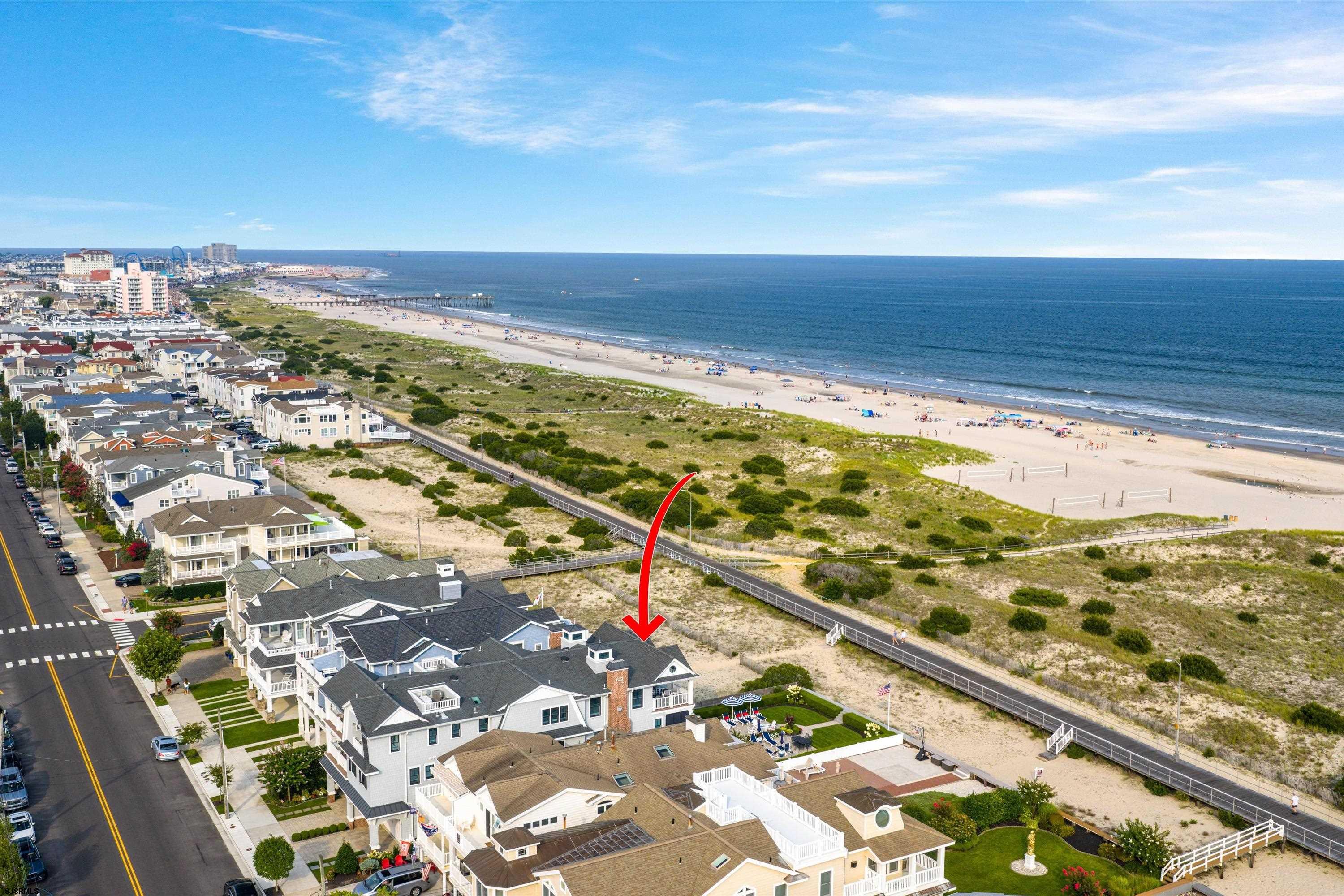 Aerial view of a beachside home marked by a red arrow, with the ocean and boardwalk beyond.