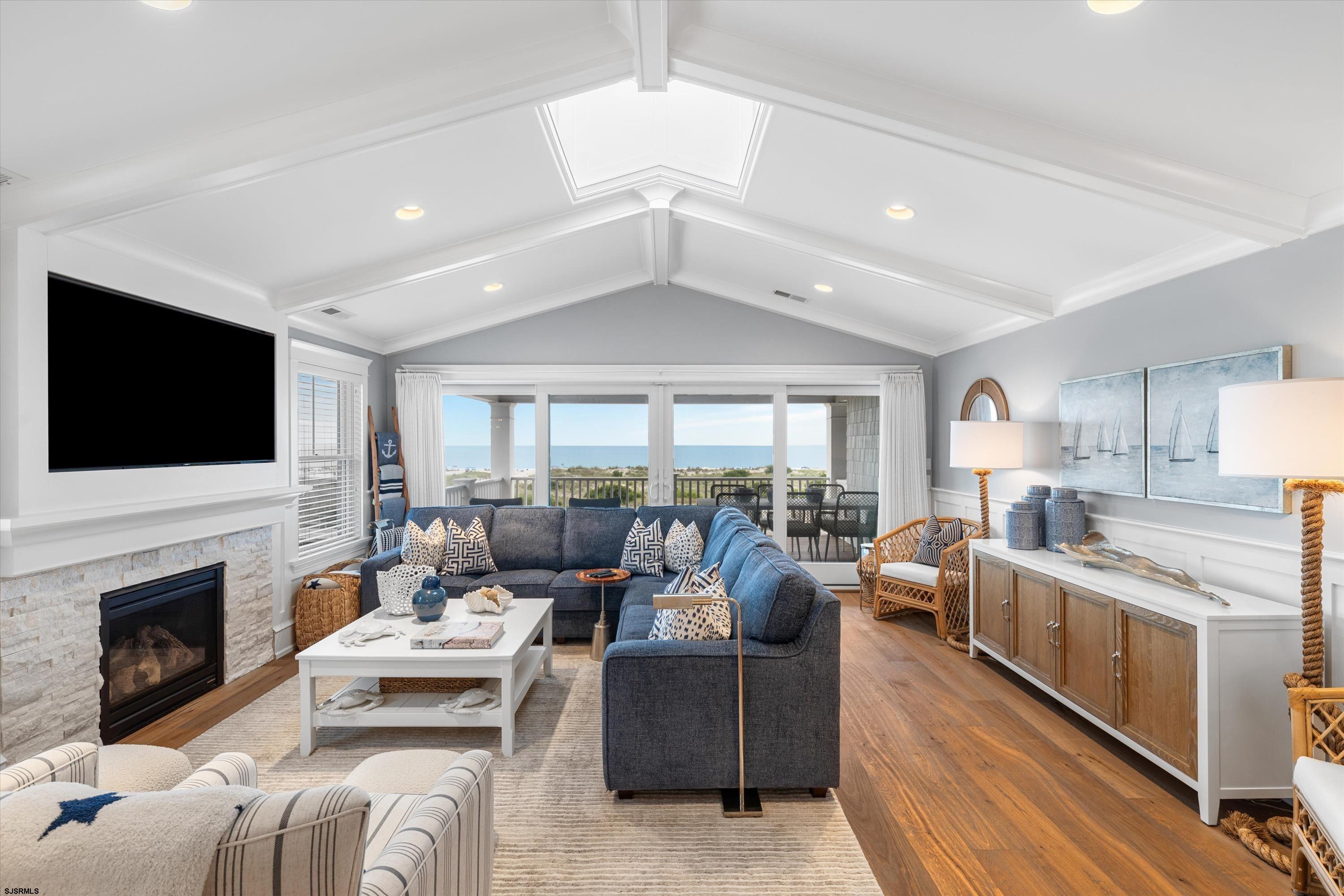 Staged living room with vaulted ceiling, fireplace, and ocean views through glass doors.