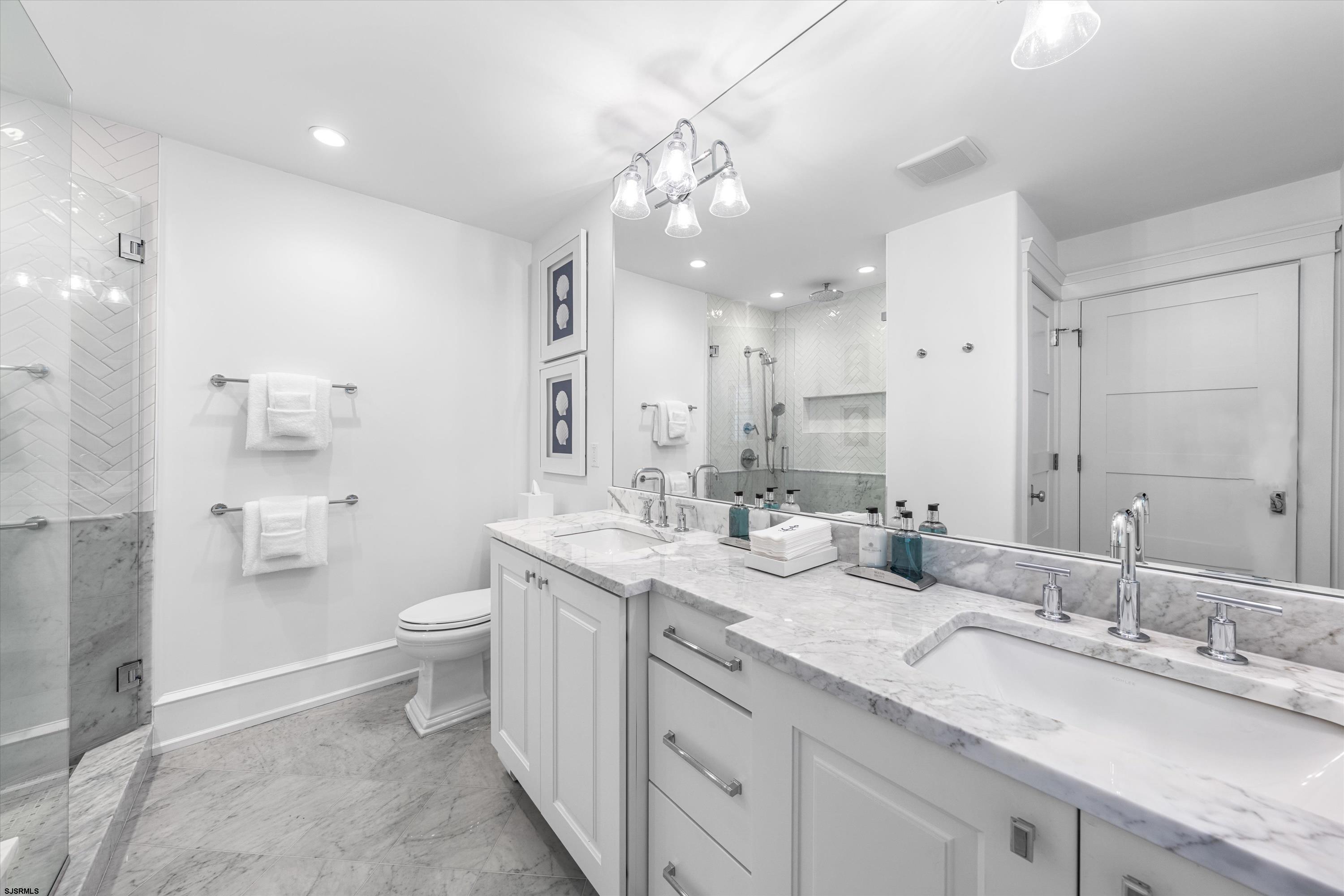 Bathroom with a marble double-sink vanity and glass shower tiled in white herringbone.