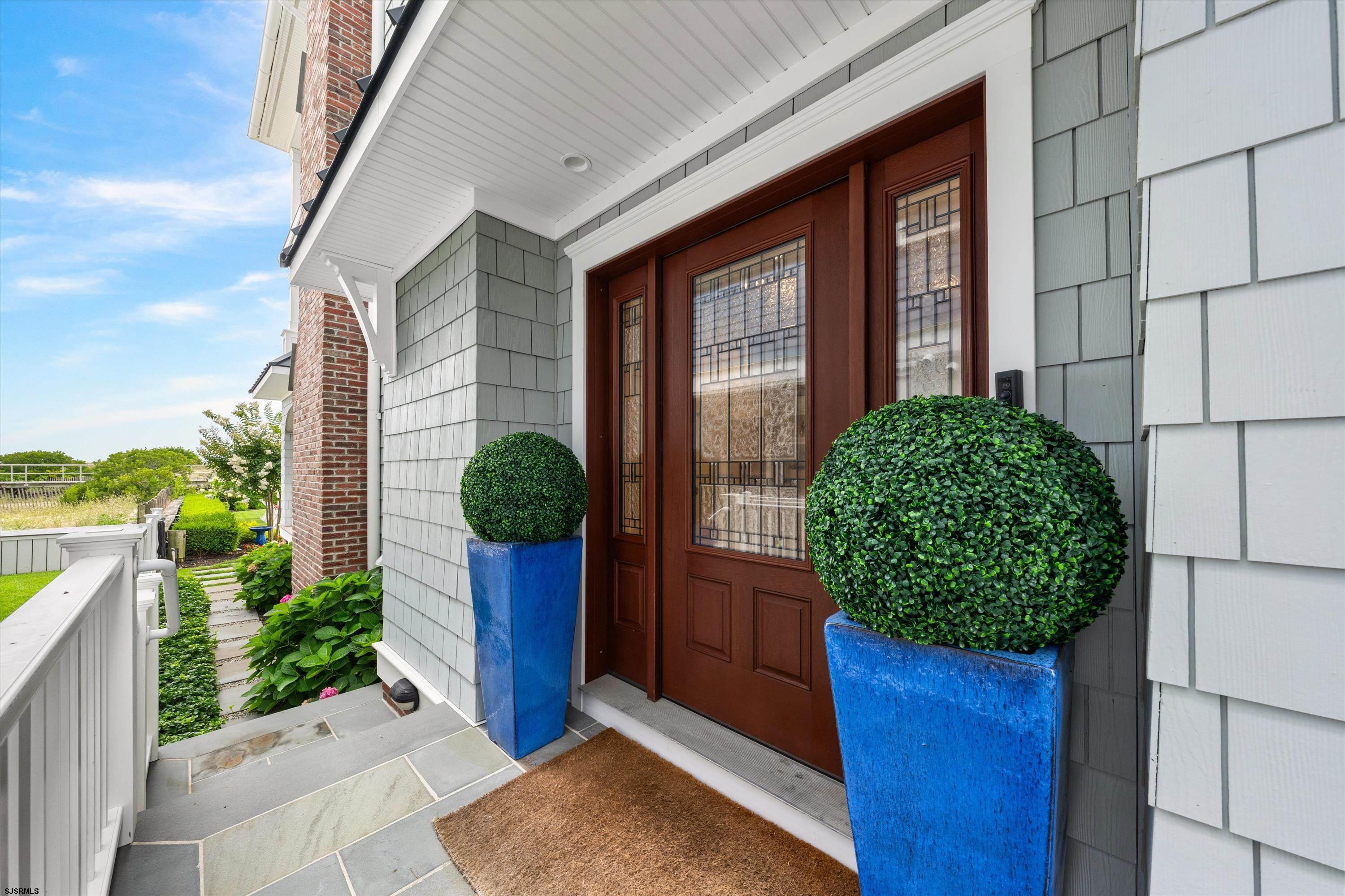 Home entrance with a decorative glass door, gray shingle siding, and shrubs in blue planters.