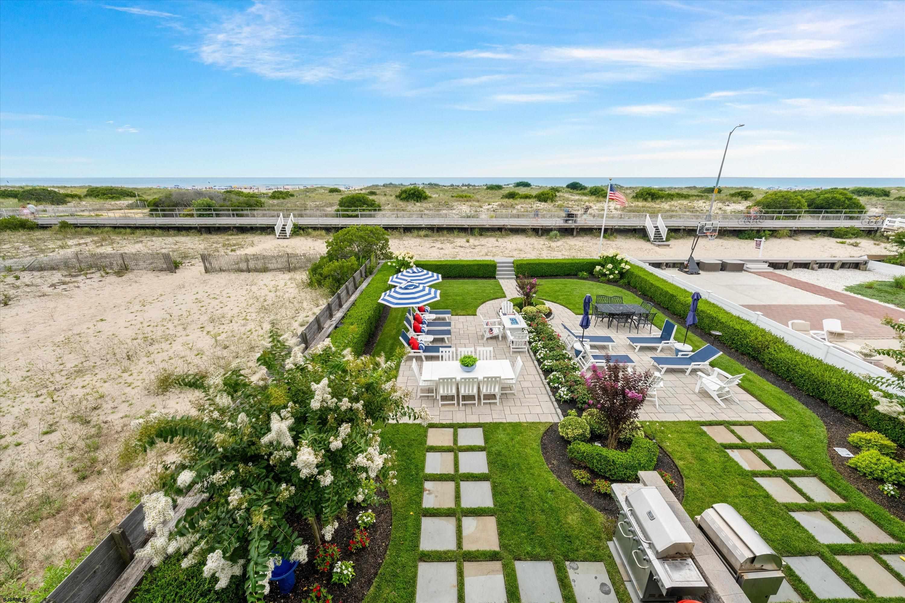 Landscaped patio with outdoor seating and grills overlooking dunes, a boardwalk, and the ocean.