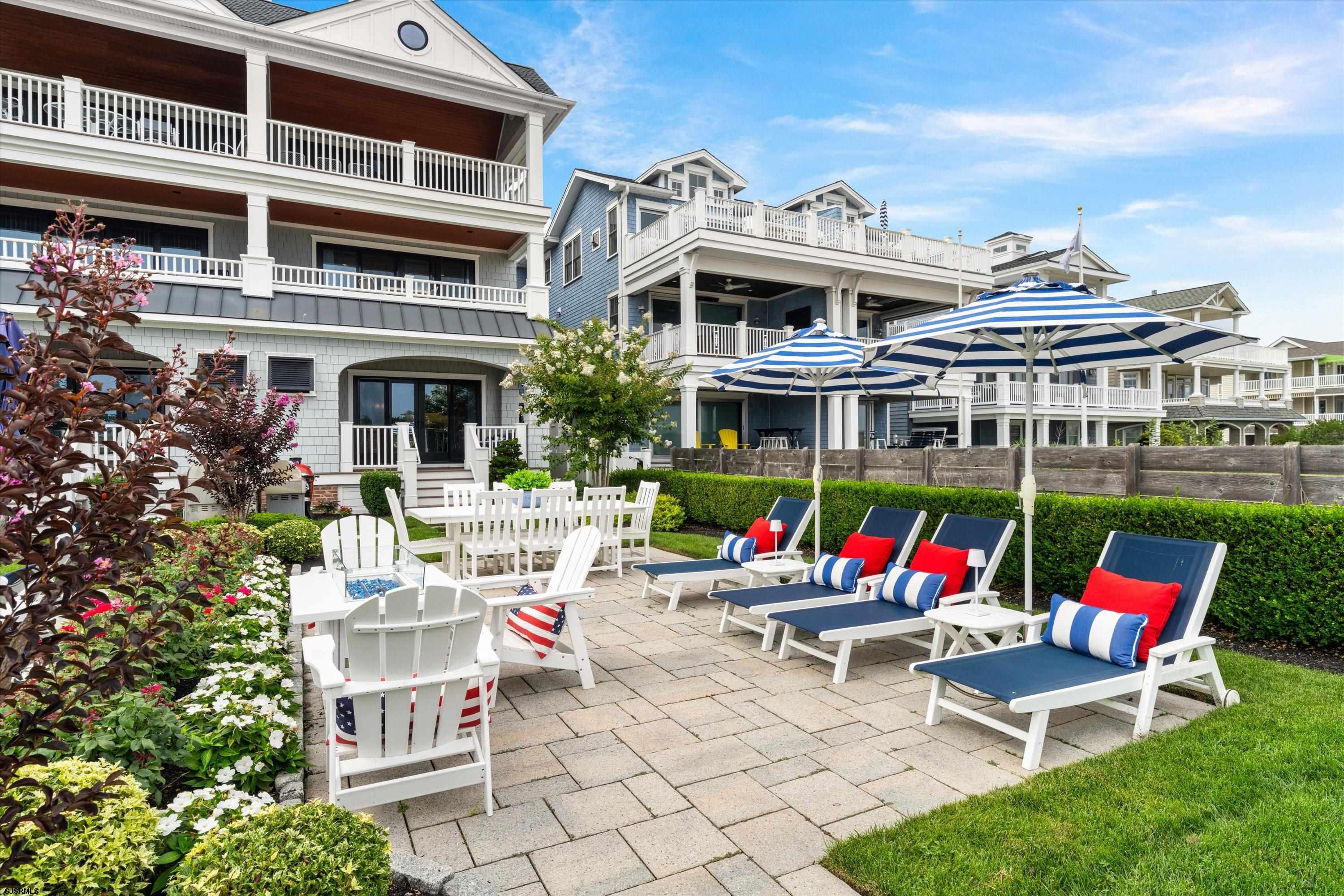 Outdoor patio courtyard with striped umbrellas, lounge chairs, dining set, and flowering landscaping.