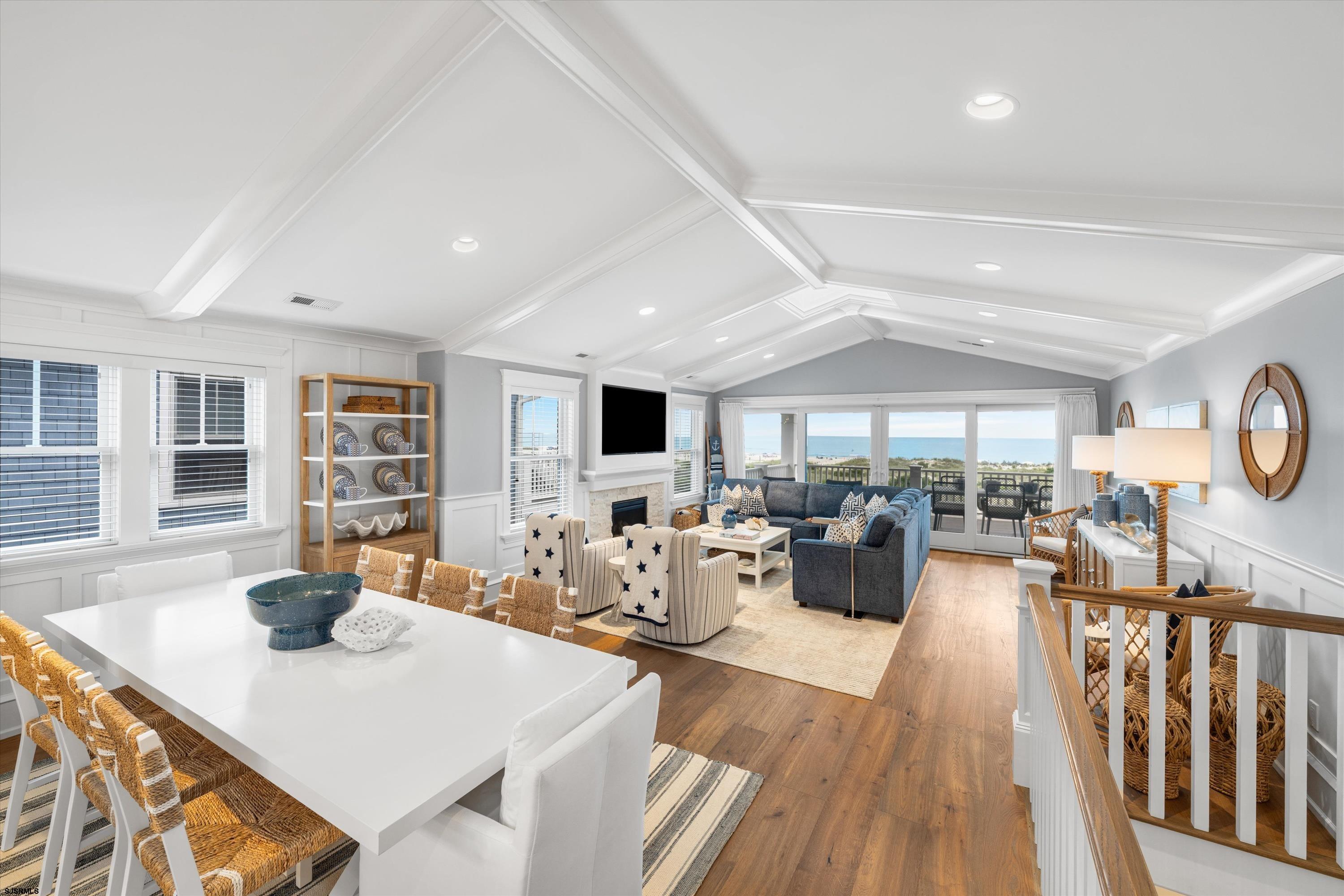 Open-plan living and dining room with a vaulted ceiling, fireplace, and ocean views through wide glass doors.