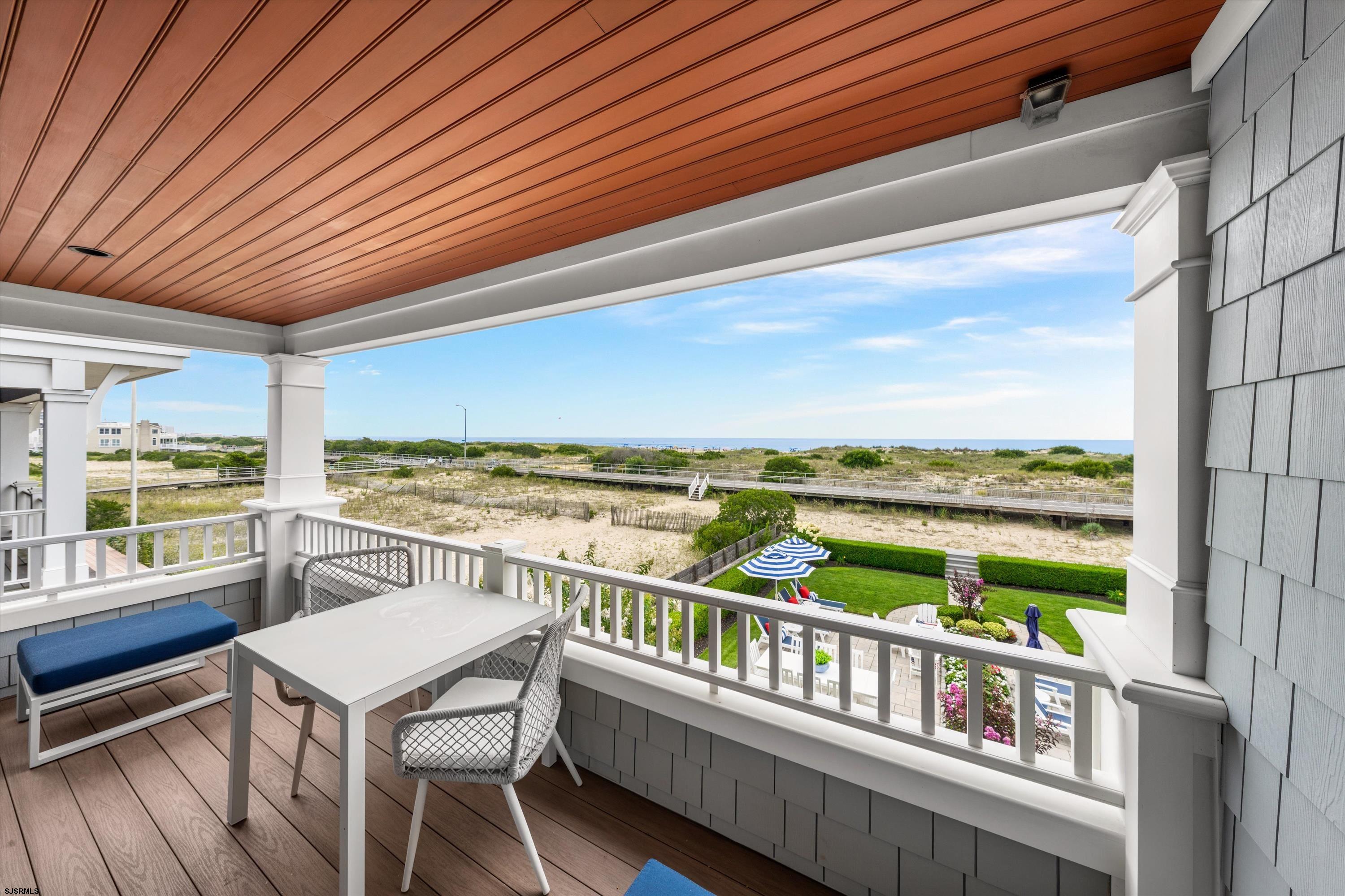 Covered balcony with outdoor dining set overlooking dunes, boardwalk, and ocean.