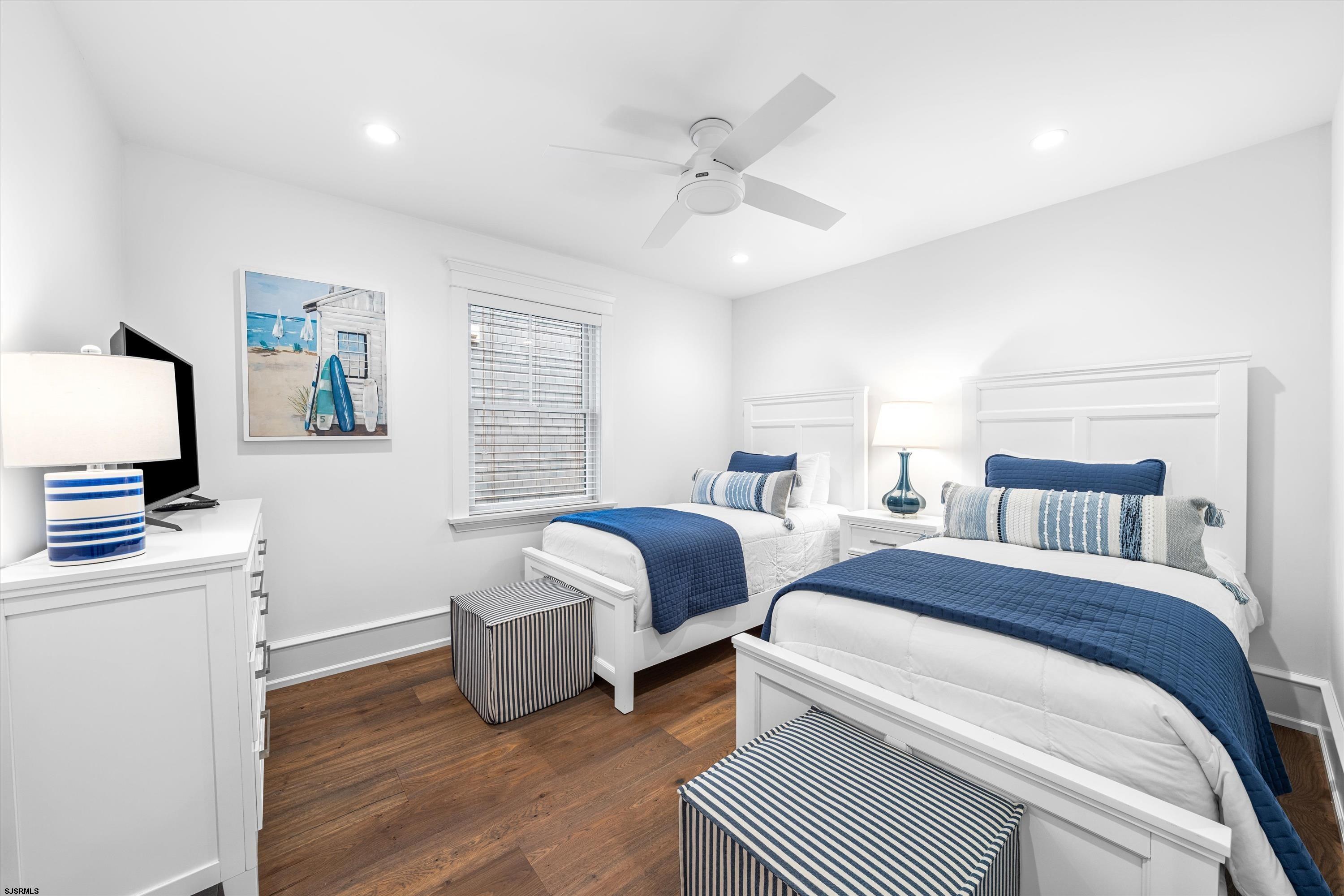 Bedroom with two white beds, navy quilts, striped accents, and hardwood floors.