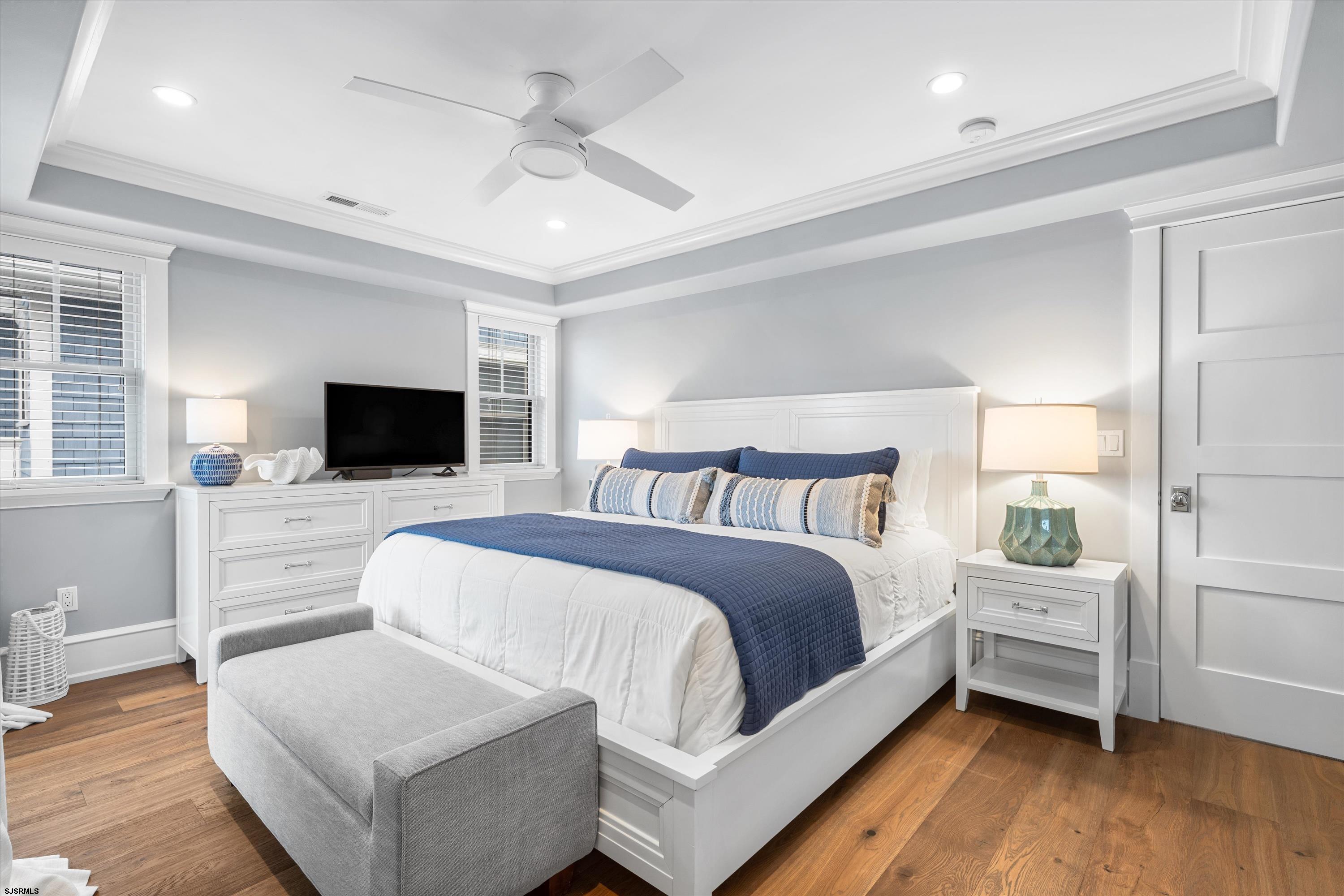 Furnished bedroom with a white bed, navy accents, hardwood floors, and a ceiling fan.
