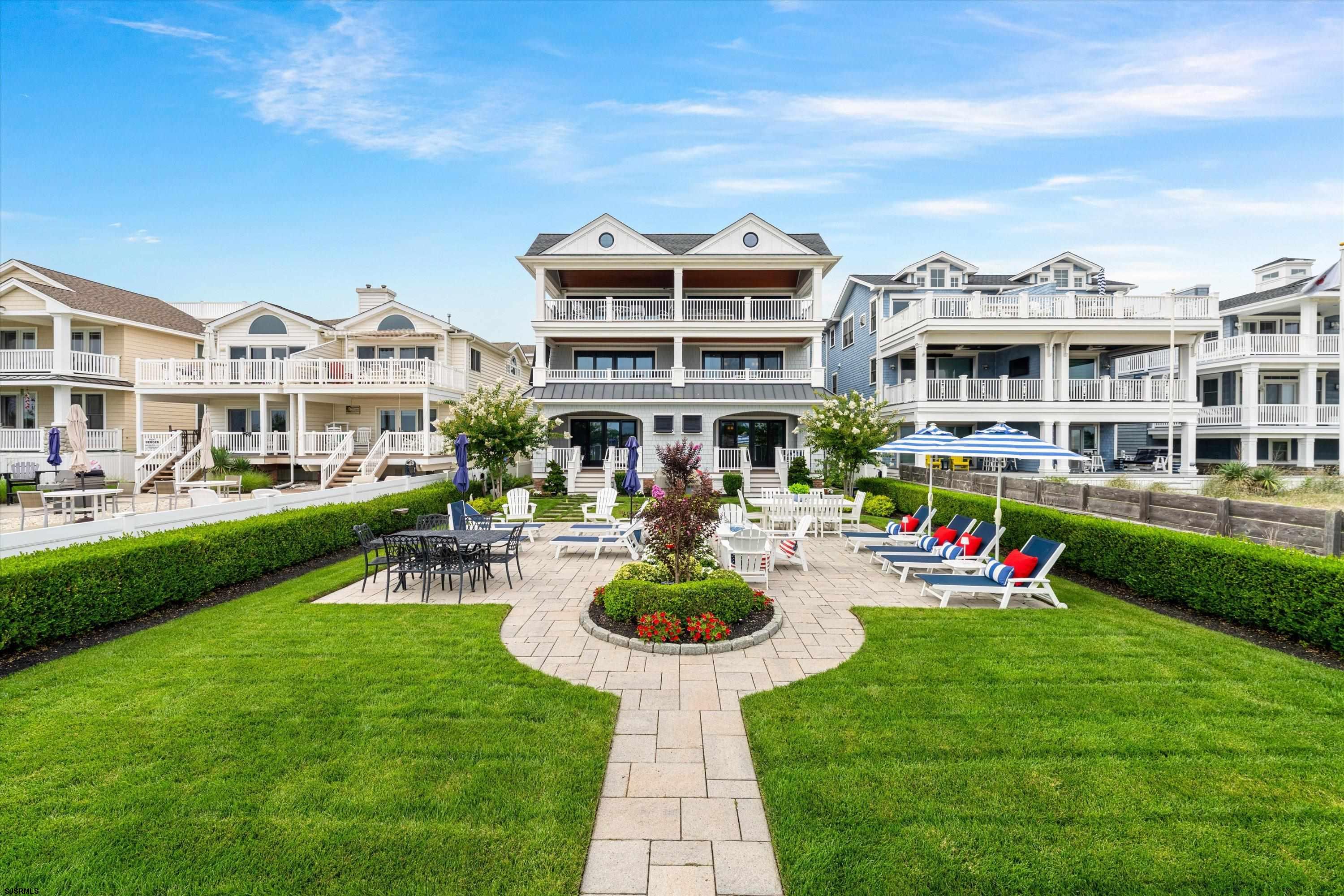 Coastal home with multiple balconies overlooking a landscaped lawn and furnished patio.