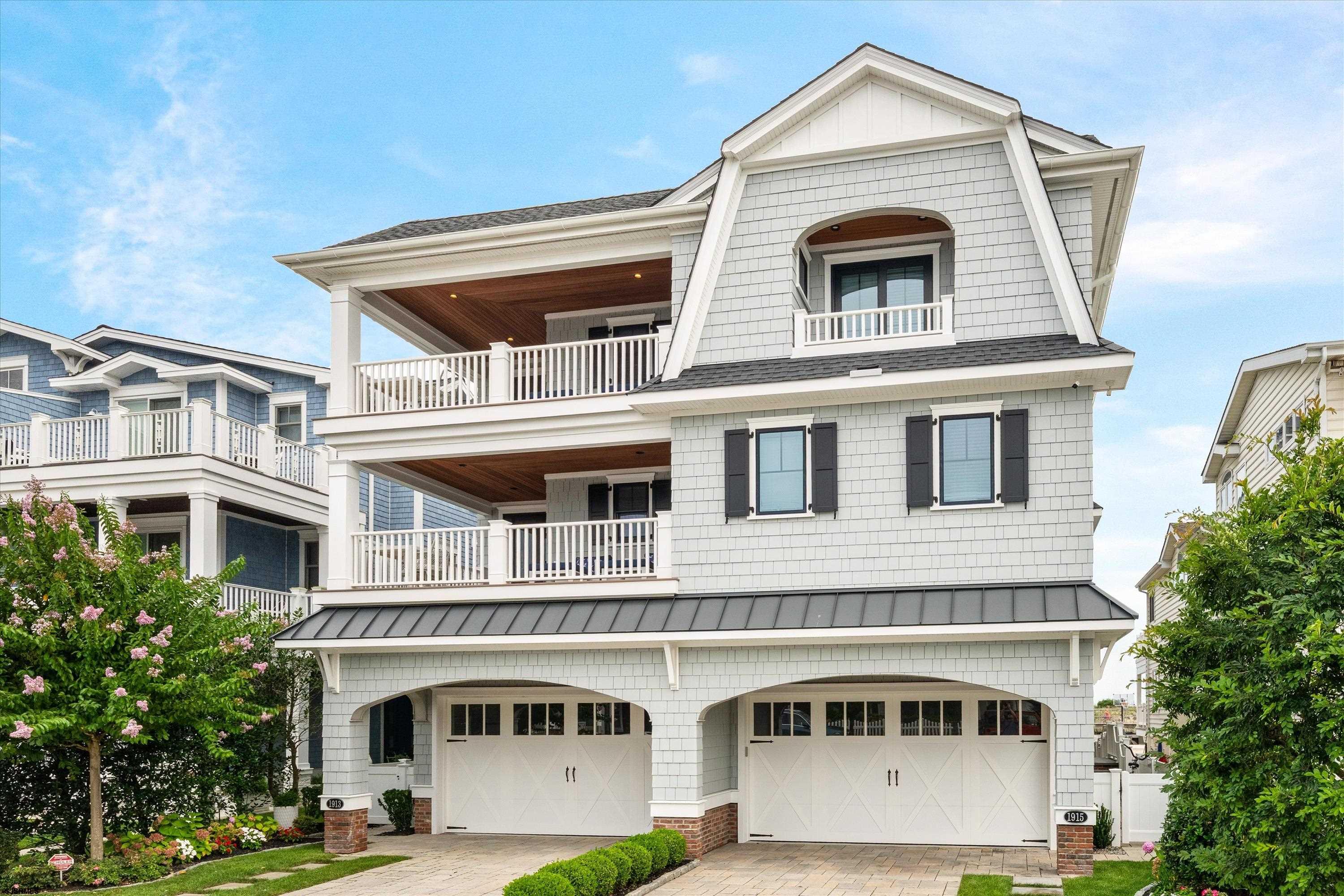 White coastal home with stacked covered balconies, dark shutters, and two garage doors.