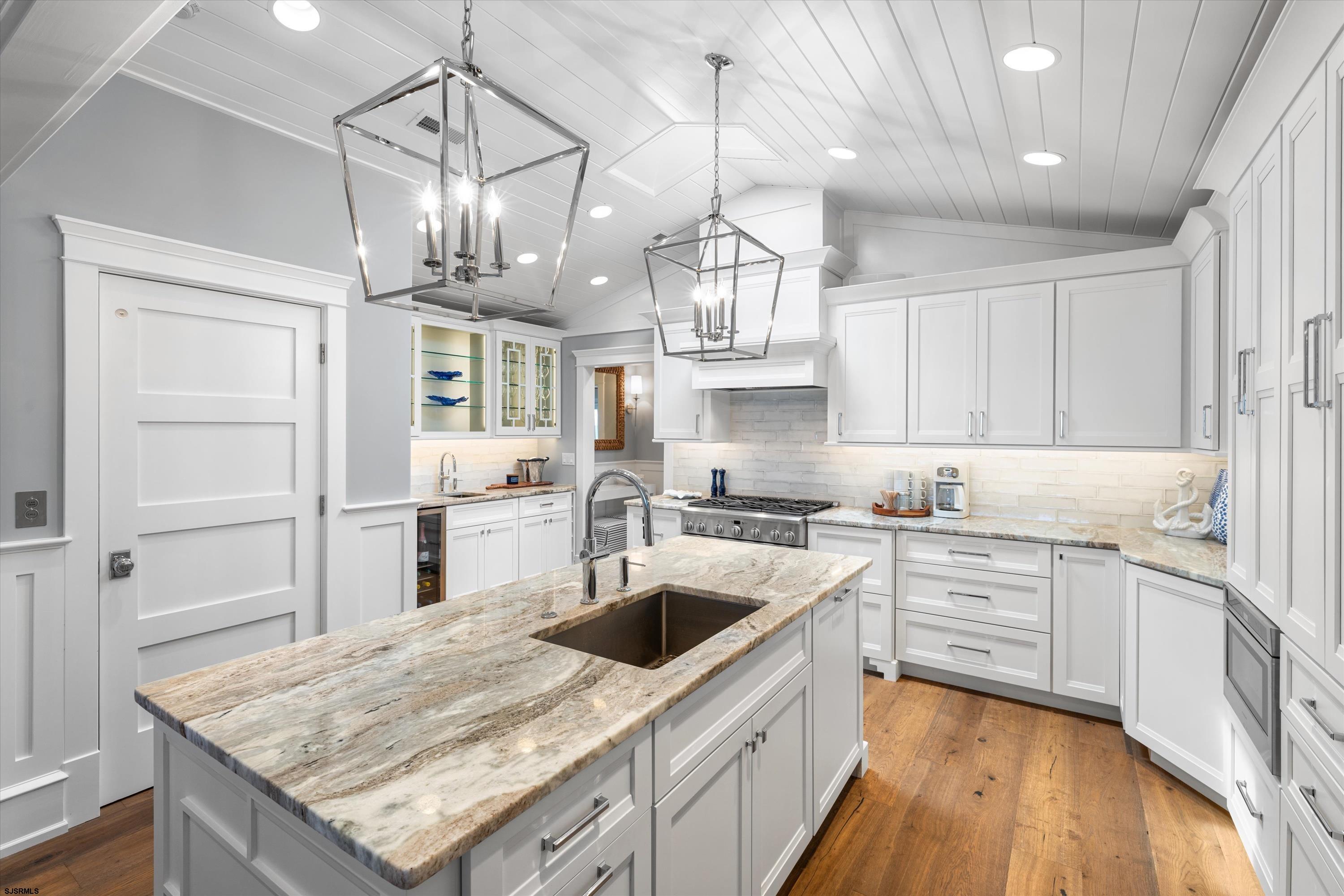 White kitchen with a large marble island, undermount sink, and stainless steel range.