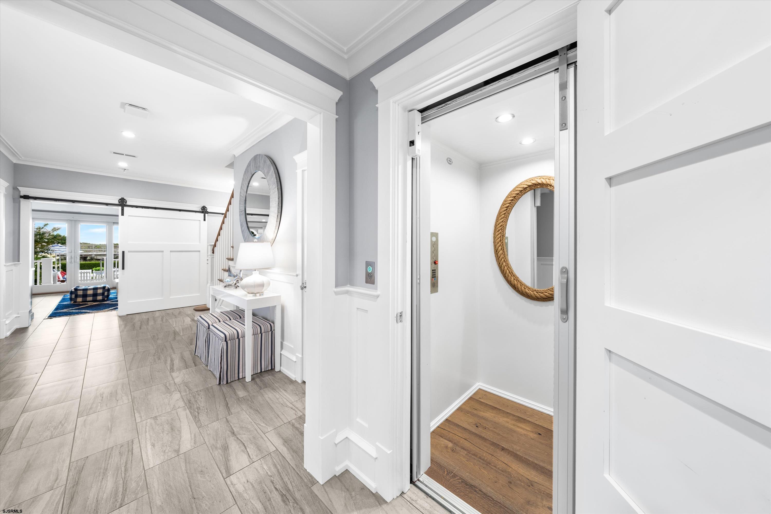 Staged foyer with an open elevator, wood flooring, and a rope-framed mirror.