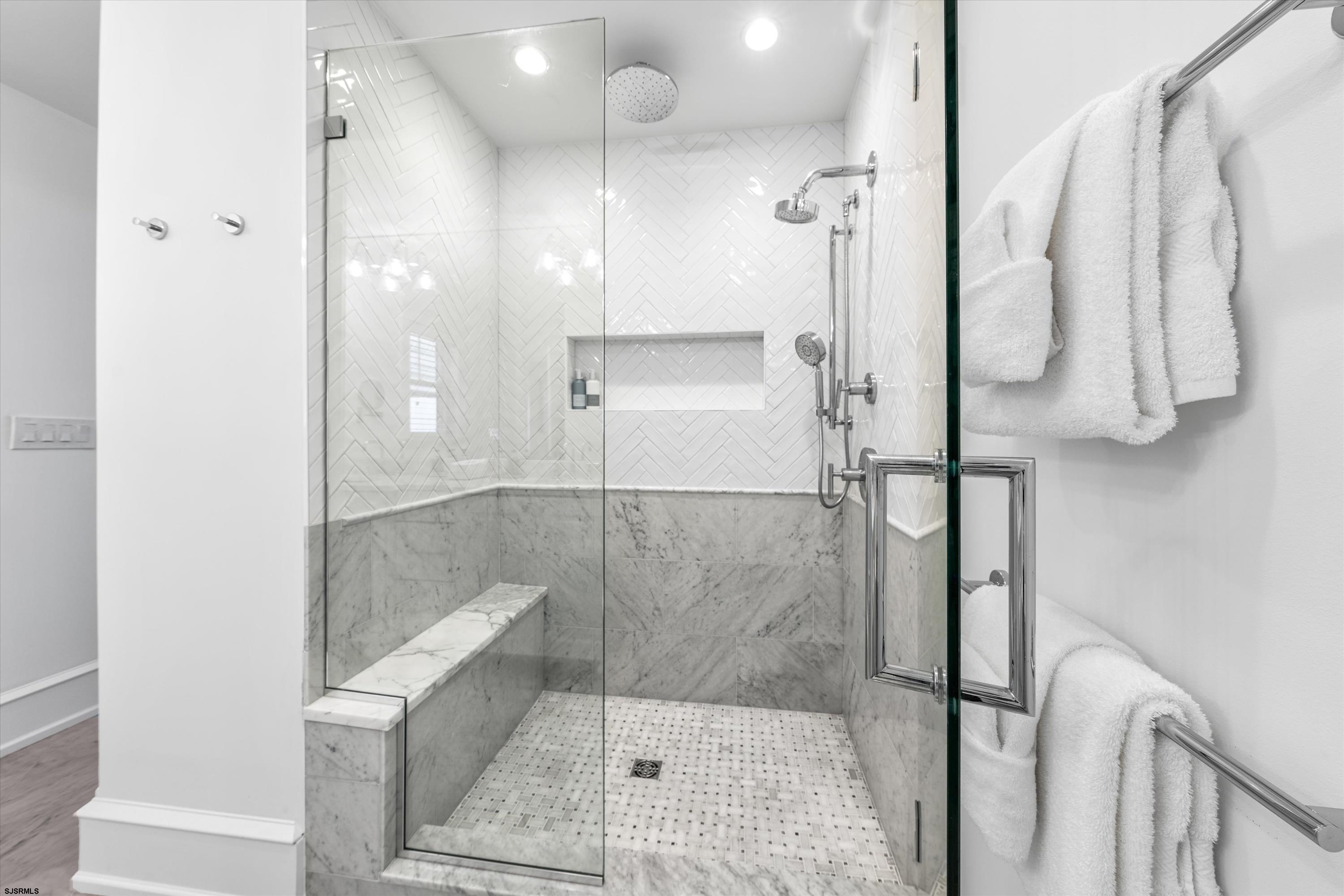 Walk-in shower with white herringbone tile, gray marble bench, and multiple shower fixtures.