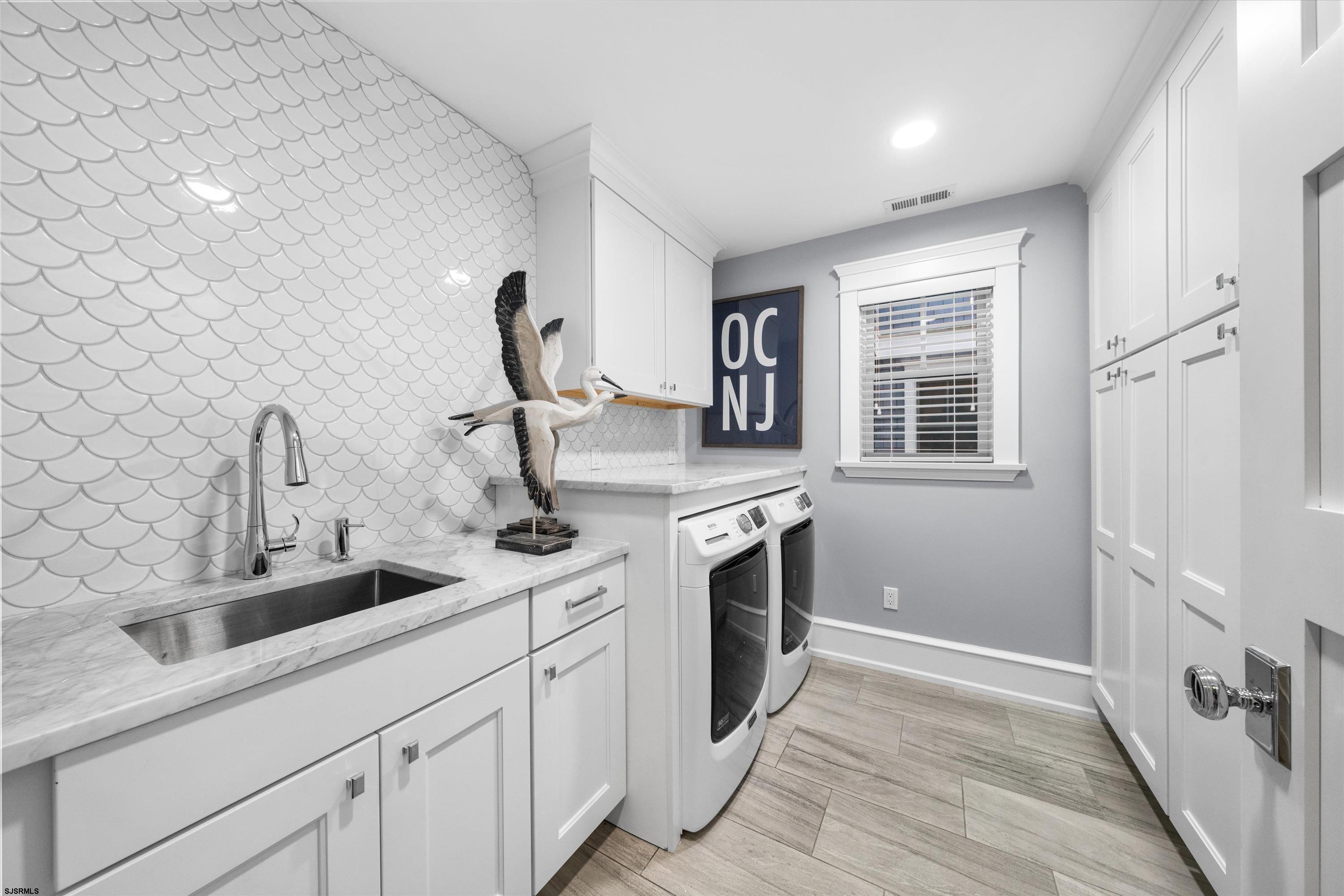 Laundry room with scalloped tile backsplash, marble-look sink counter, washer and dryer, and white built-in cabinets.