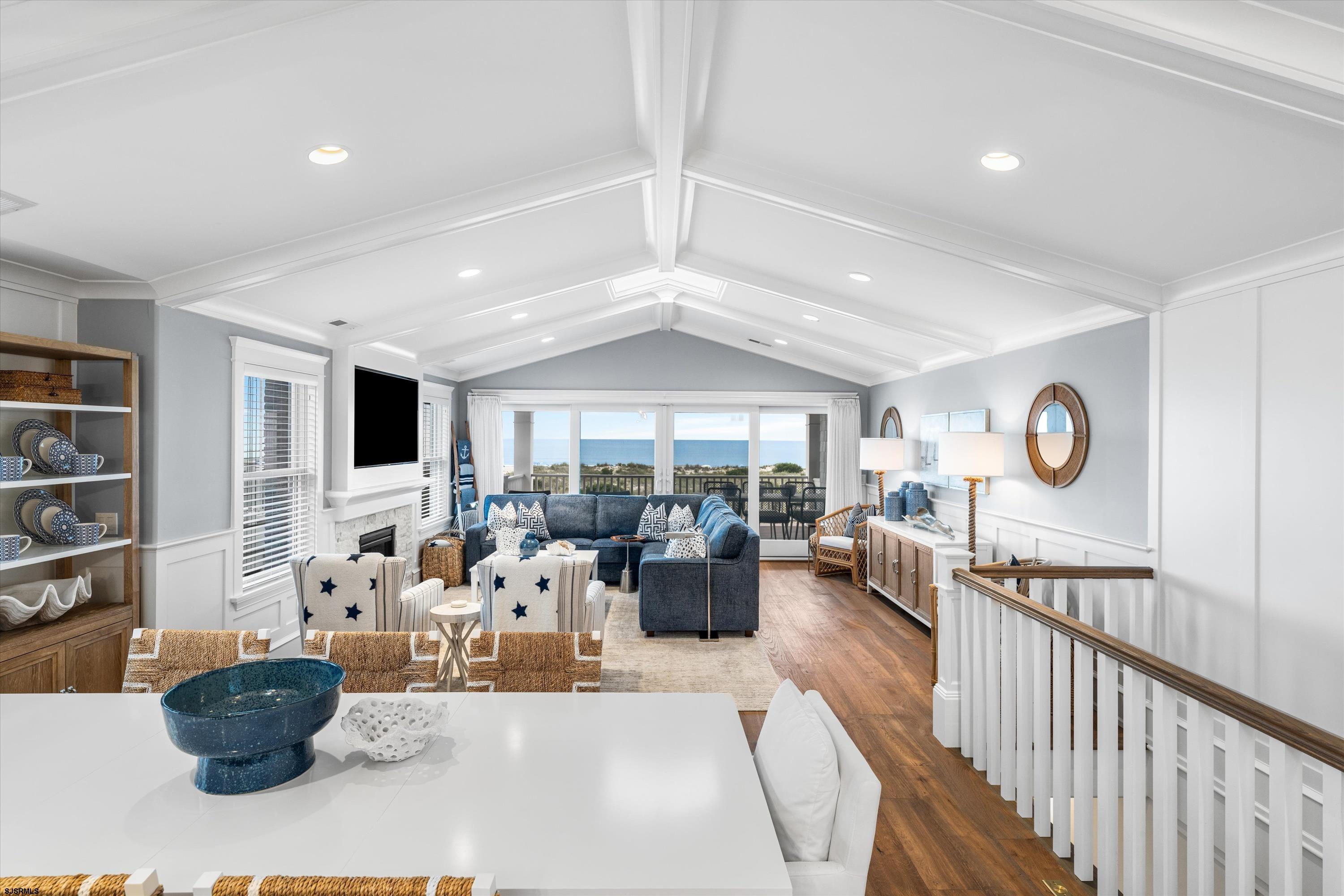 Coastal living room with vaulted ceiling, blue sectional, fireplace, and ocean view through large windows.