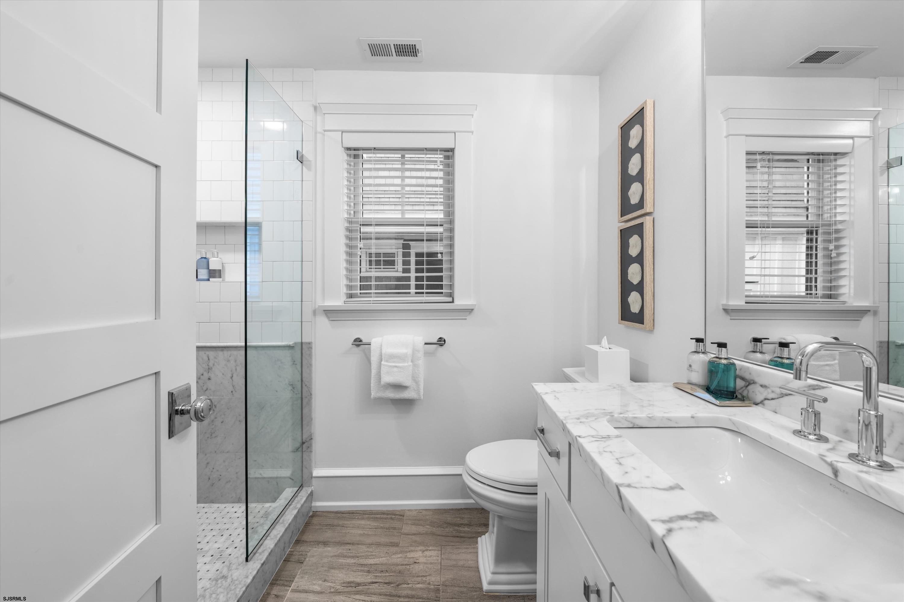 Bright bathroom with a glass shower, marble vanity, and wood-look tile floor.