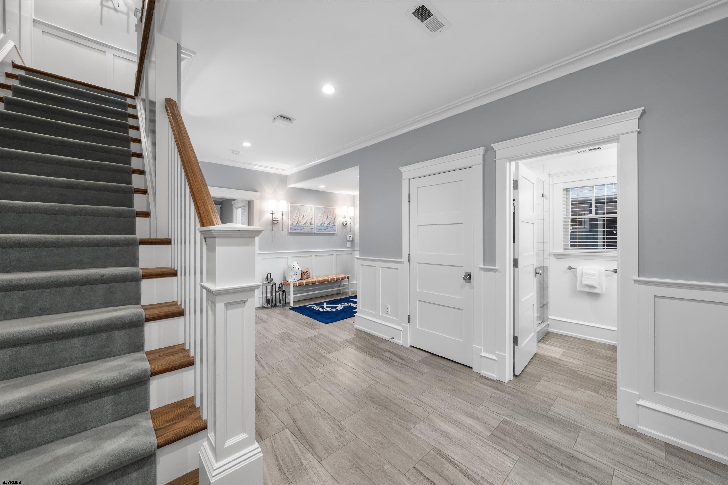 Entry hall with carpeted staircase, wood treads, tiled floor, and open bathroom doorway.