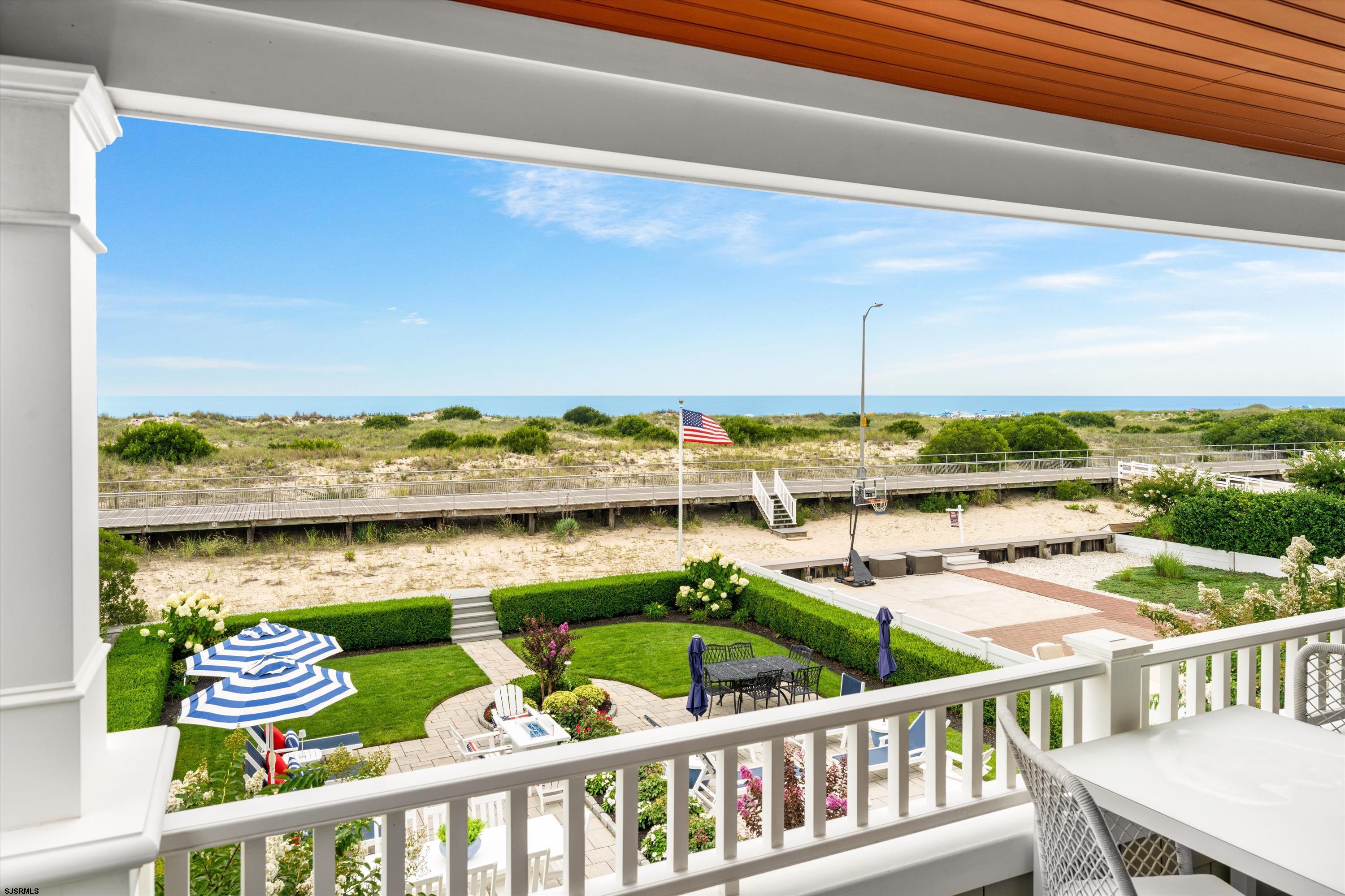 Balcony overlooking a landscaped garden, beach boardwalk, dunes, and ocean.