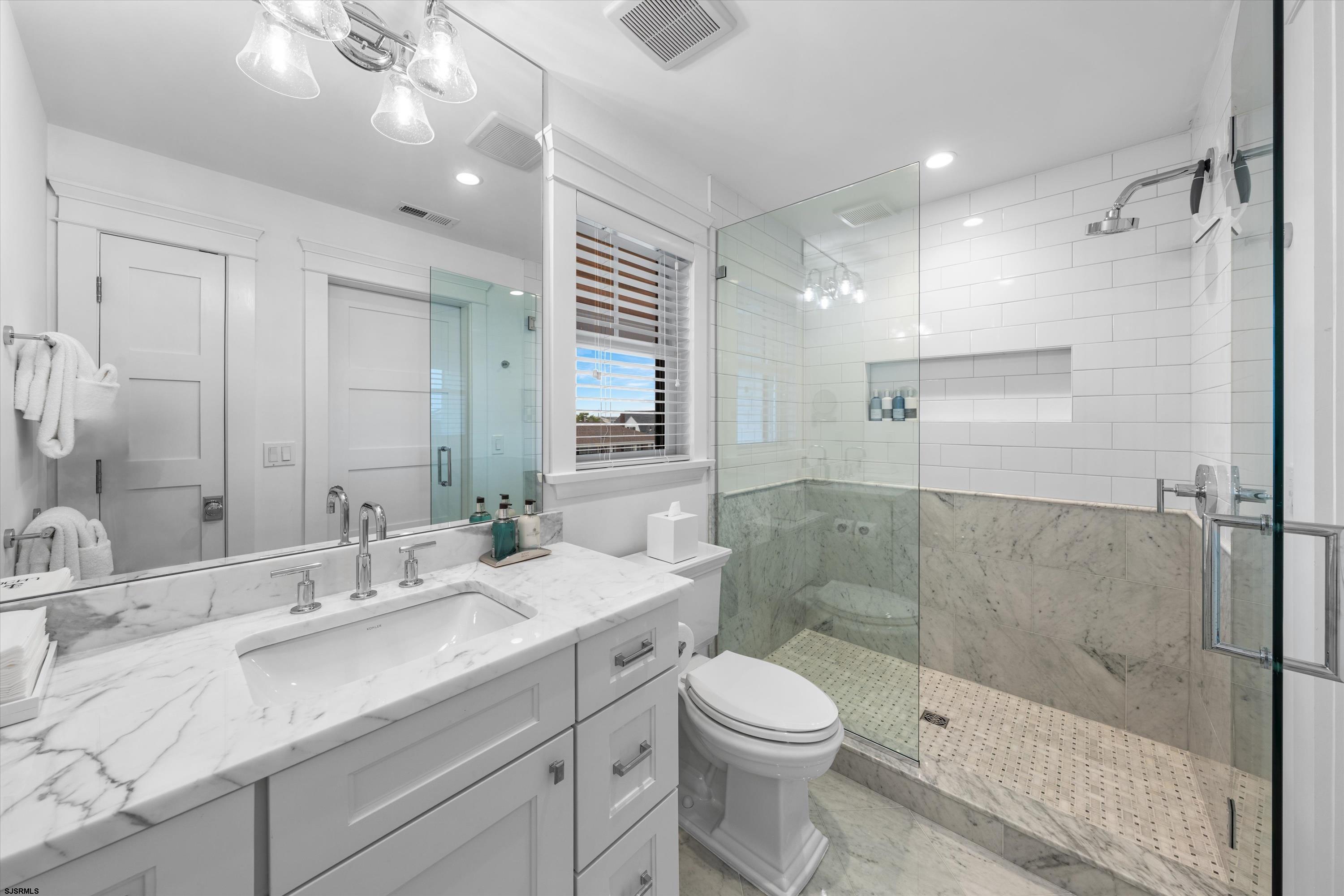 Bathroom with a marble vanity and spacious glass-enclosed shower featuring subway tile and a mosaic floor.