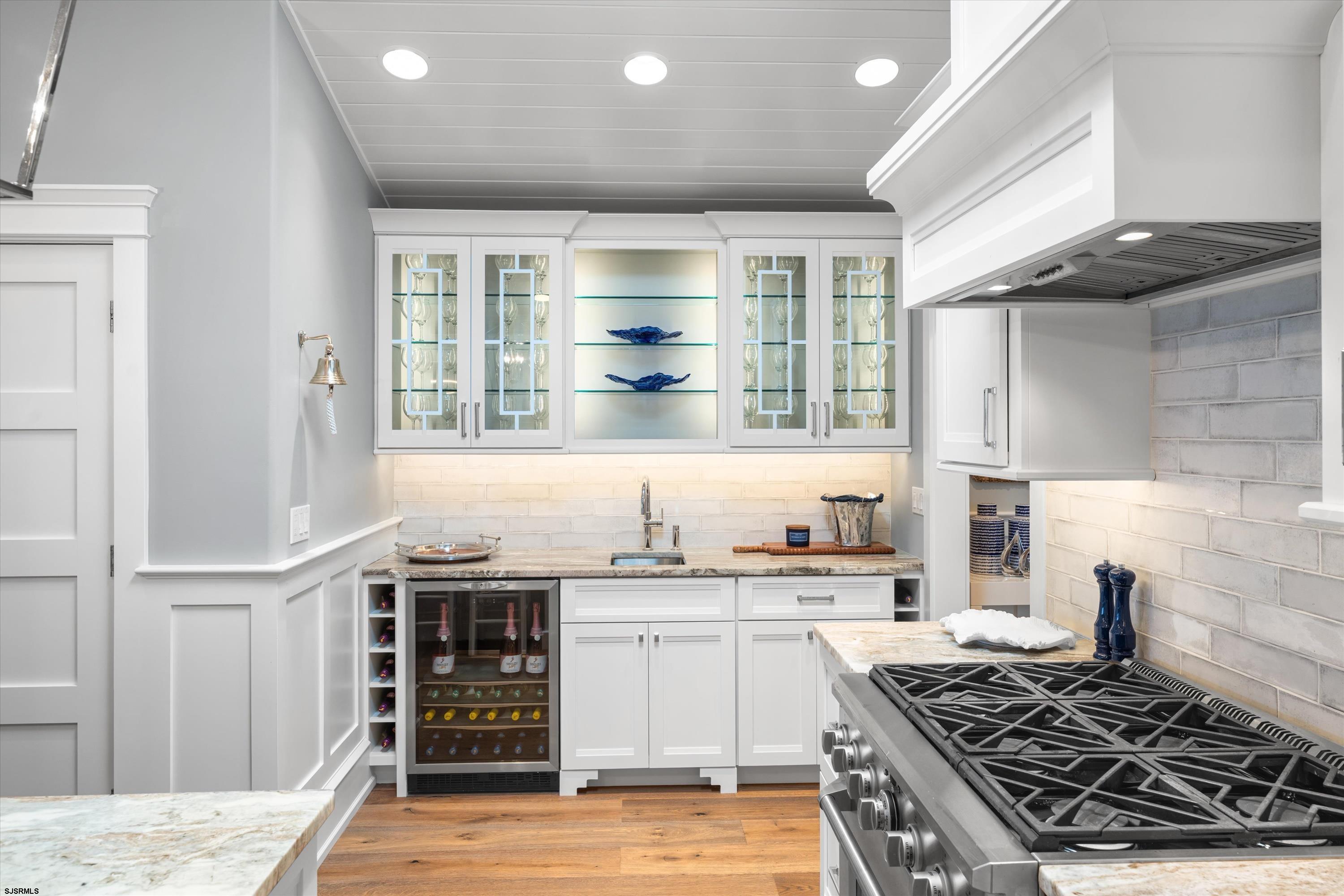 Kitchen with white cabinetry, glass-front display shelves, and a large stainless gas range.