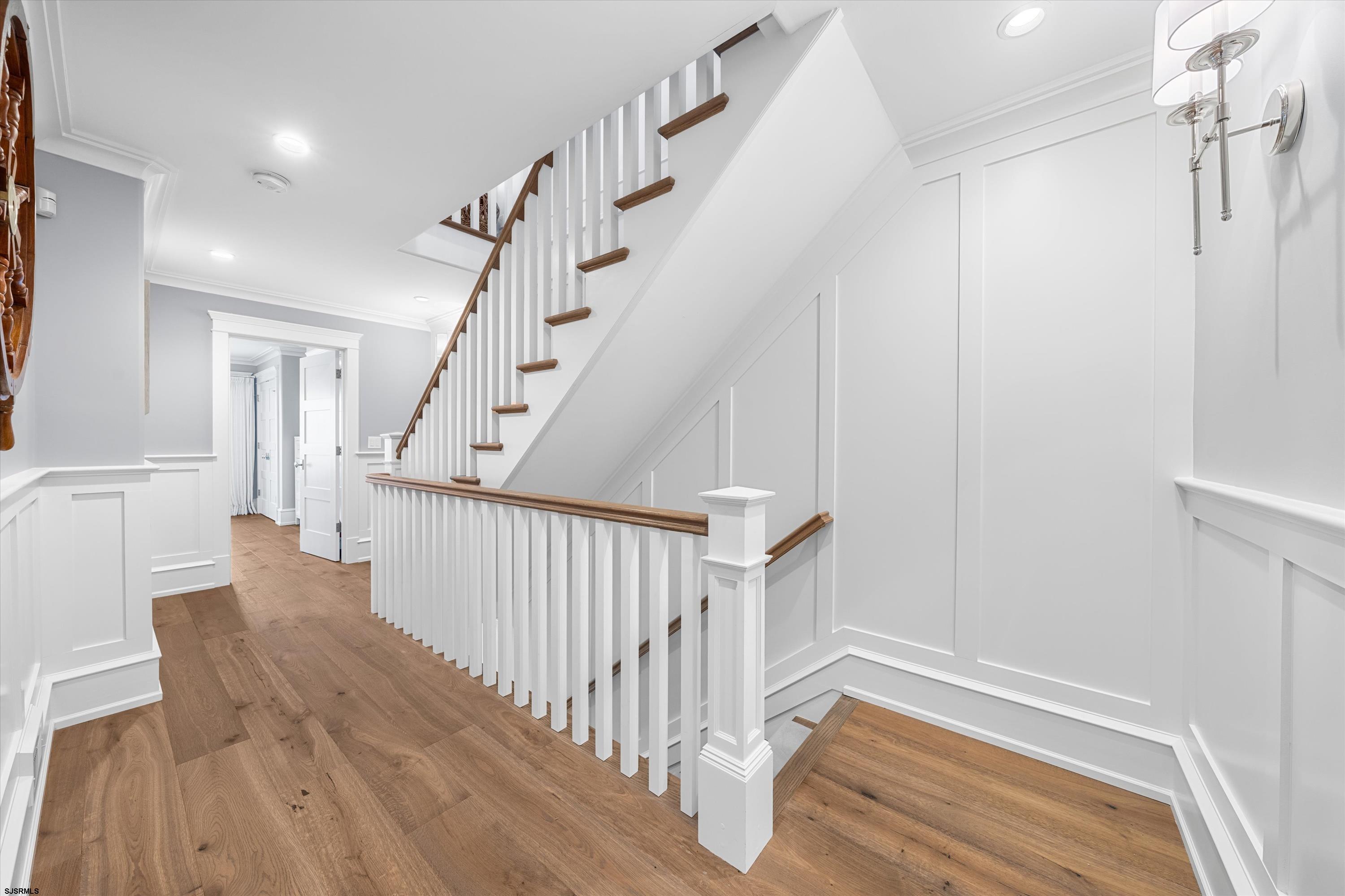Hallway with a white paneled staircase, wood handrails, and warm wood flooring.