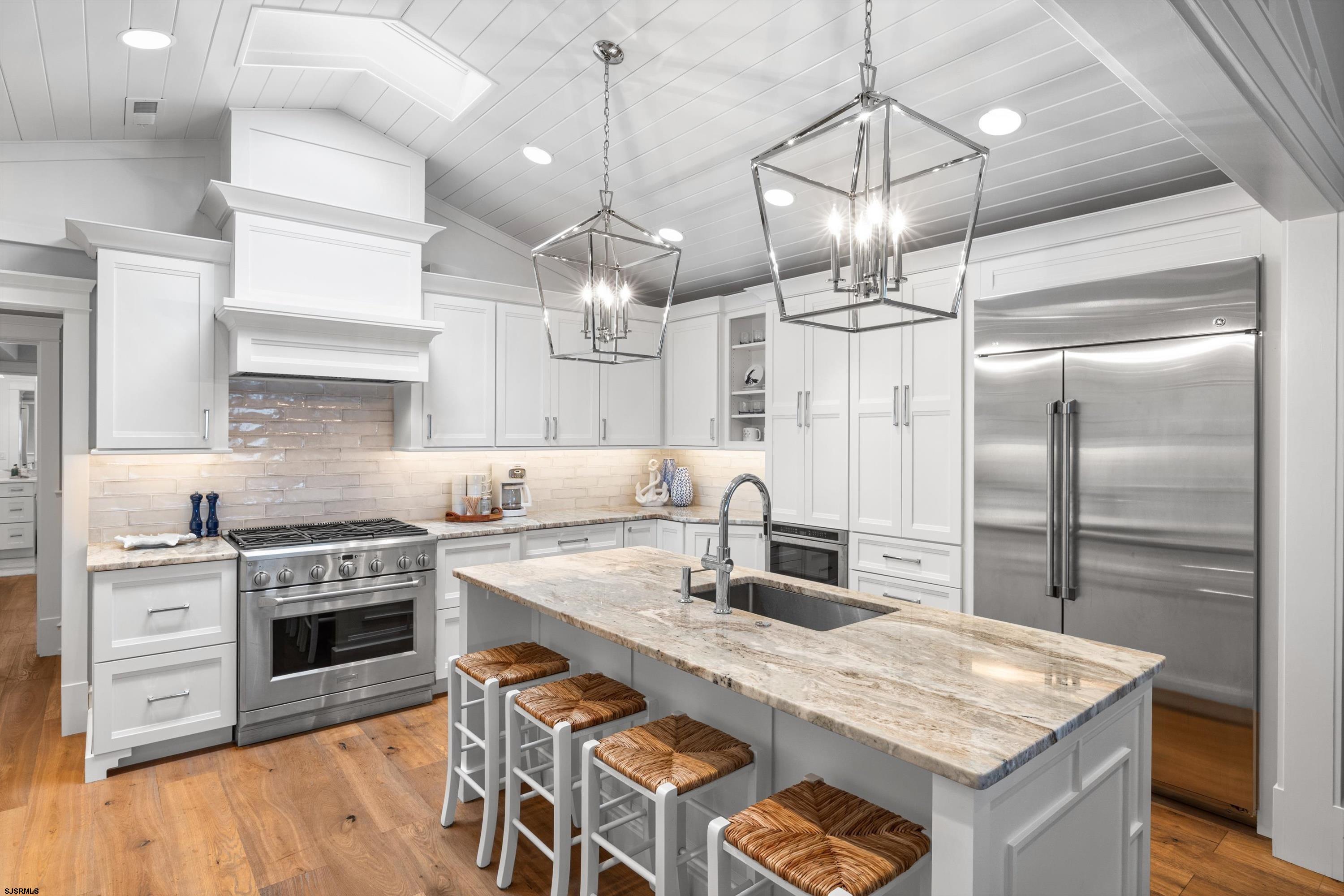 White kitchen with a large stone island, stainless steel appliances, and two geometric pendant lights.